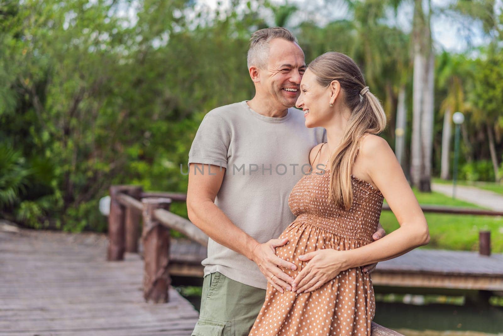 A happy, mature couple over 40, enjoying a leisurely walk in a park, their joy evident as they embrace the journey of pregnancy later in life.