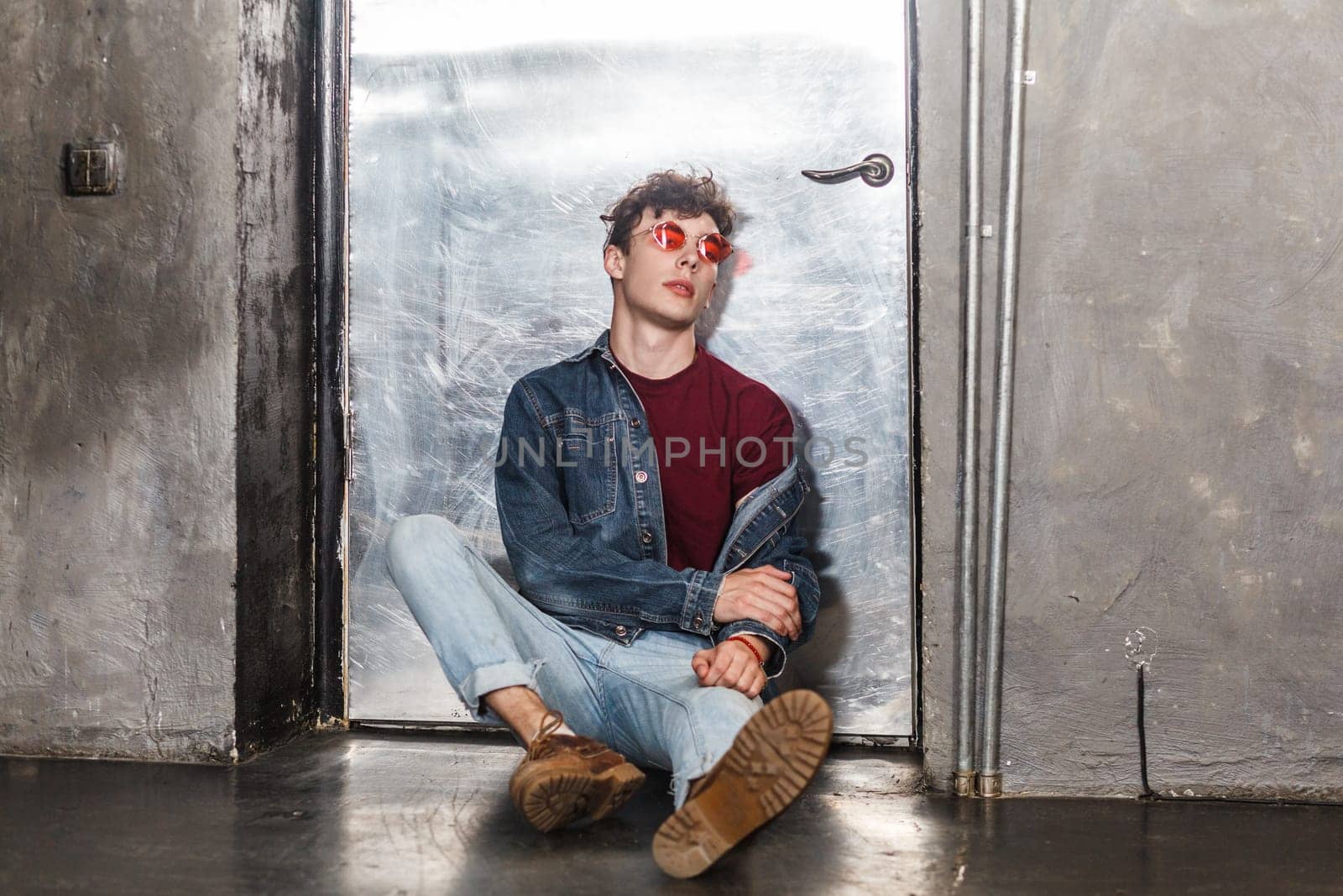 Calm relaxed model man in bright red sunglasses and denim casual style, sitting near metallic door, by Khosro1