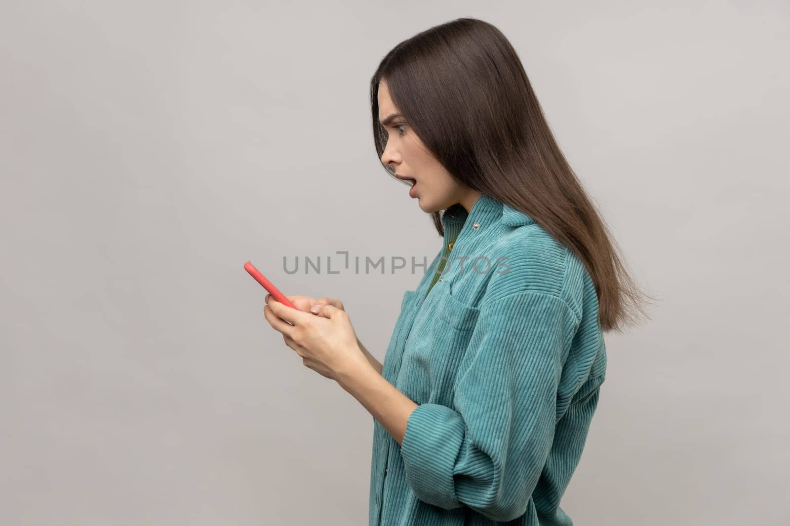 Side view of shocked pretty woman reading message on smartphone with open mouth, using mobile device by Khosro1