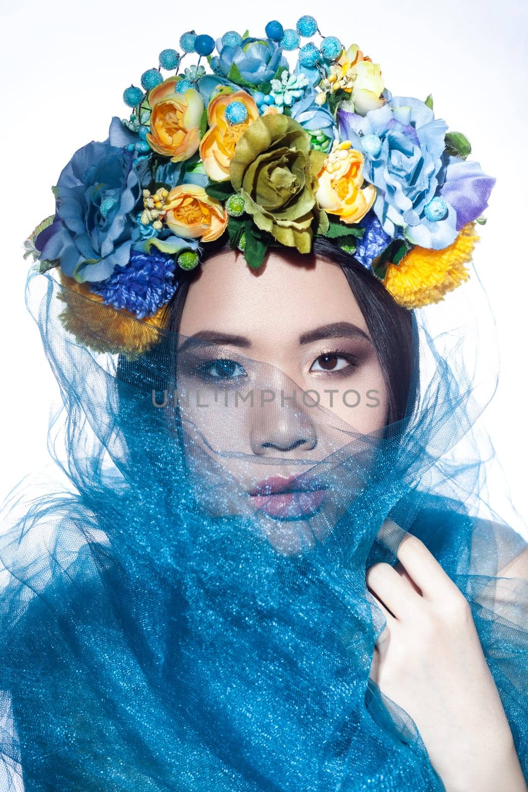 Closeup portrait of sensual attractive beautiful woman with floral hat and blue veil, hiding her face, looking at camera. Indoor studio shot isolated on gray background.