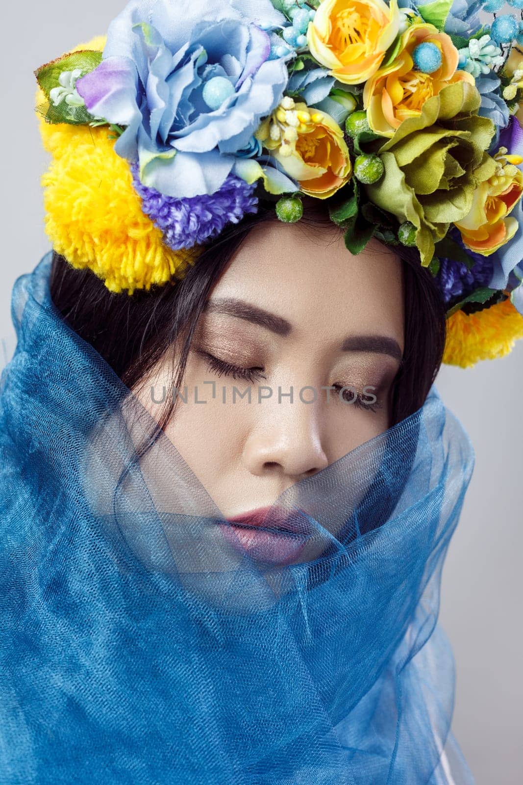 Portrait of sensual attractive woman with beautiful makeup , dark hair, with floral hat and blue veil, posing with closed eyes, expressing gentle. Indoor studio shot isolated on gray background,