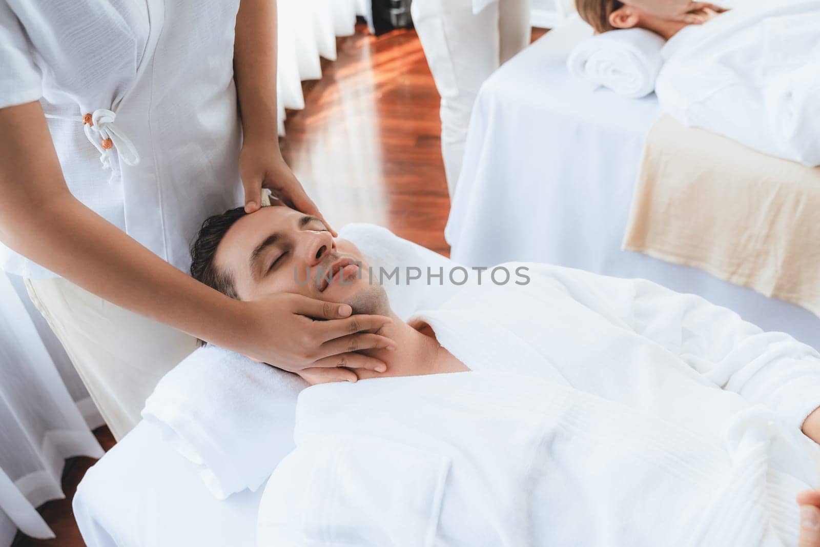 Caucasian couple enjoying relaxing anti-stress head massage and pampering facial beauty skin recreation leisure in dayspa modern light ambient at luxury resort or hotel spa salon. Quiescent