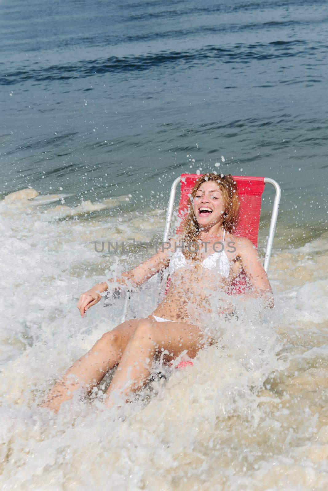 Woman in beach chair is surprised by wave