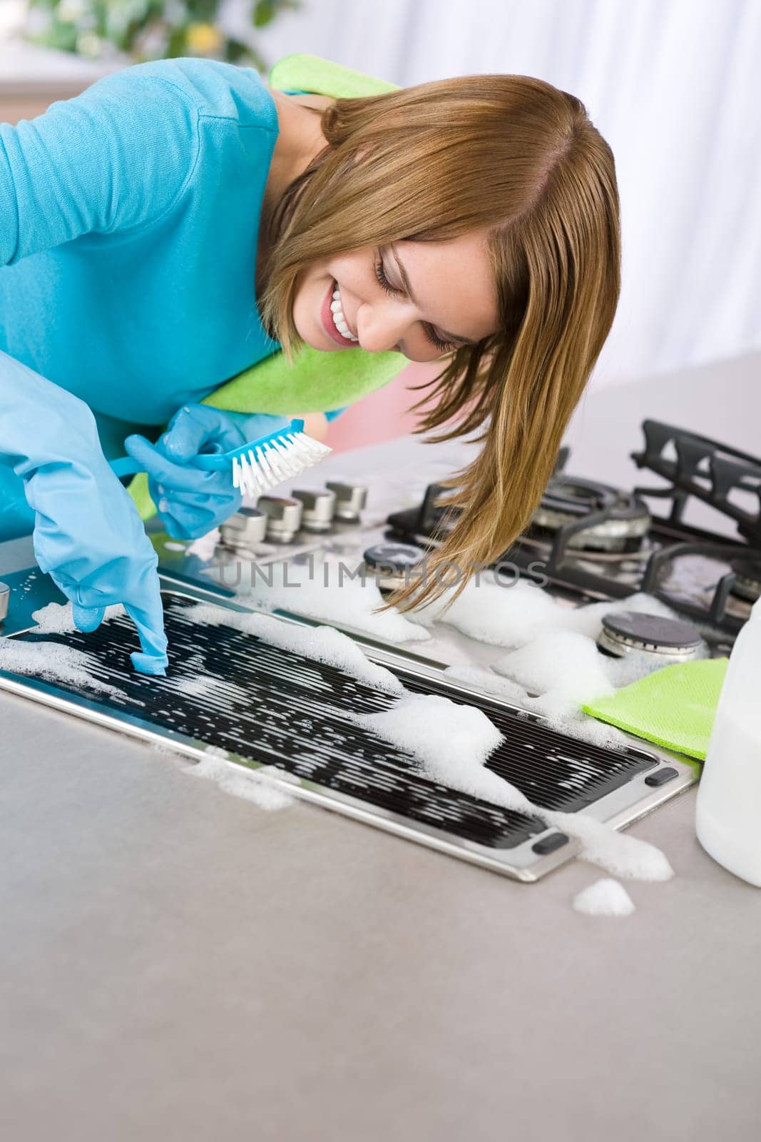 Young woman cleaning stove in kitchen