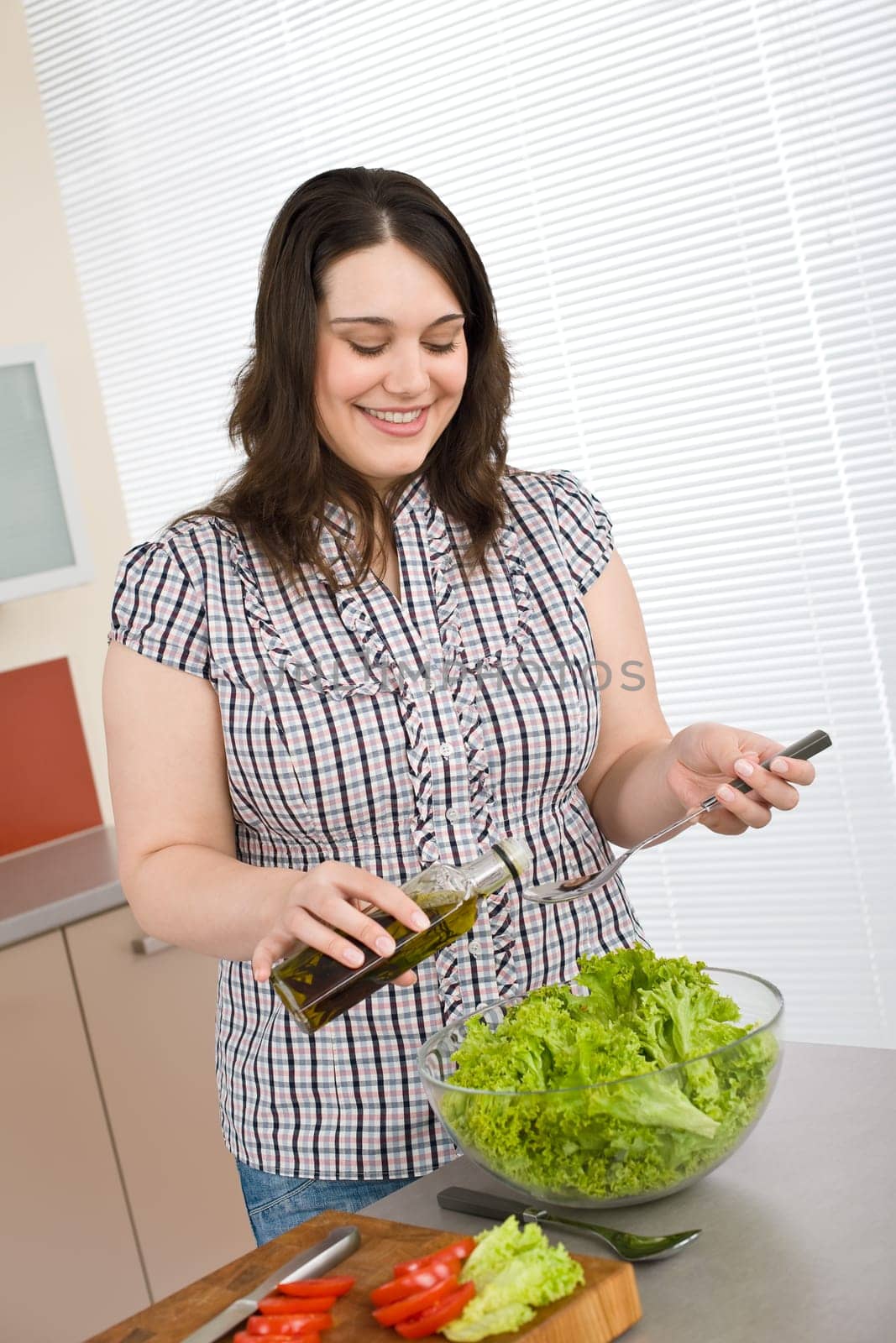 Cook - Plus size happy woman preparing salad in kitchen