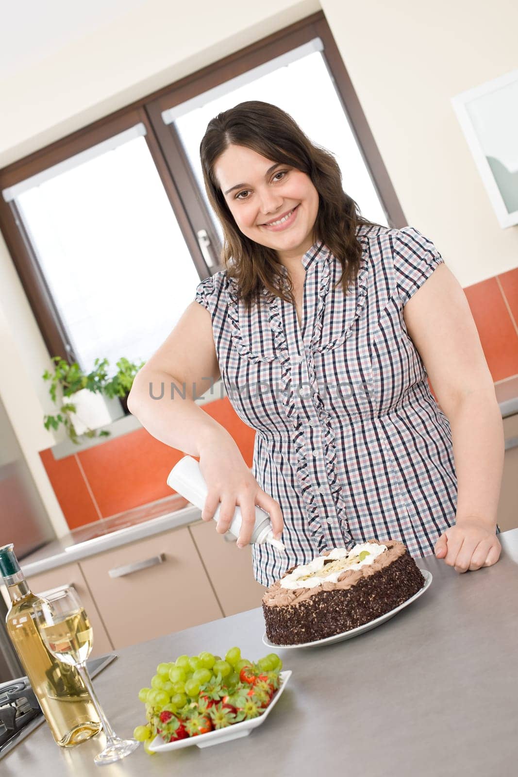Happy plus size woman with chocolate cake and cream in kitchen