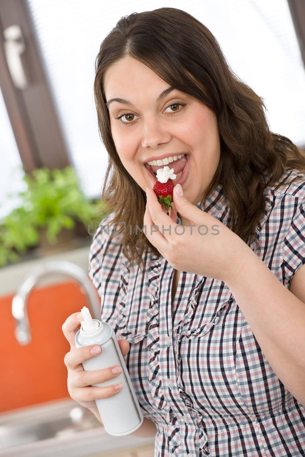 Plus size woman with whipped cream on strawberry in kitchen