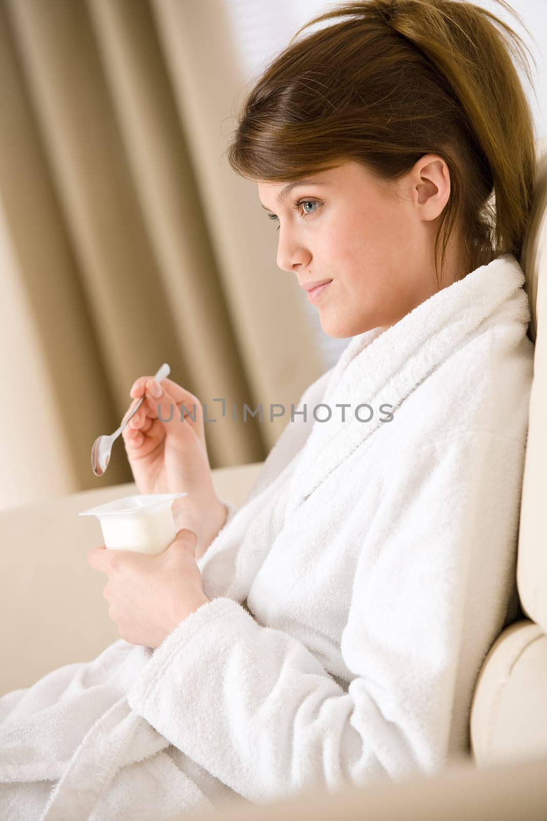 Young woman in bathrobe eating yogurt
