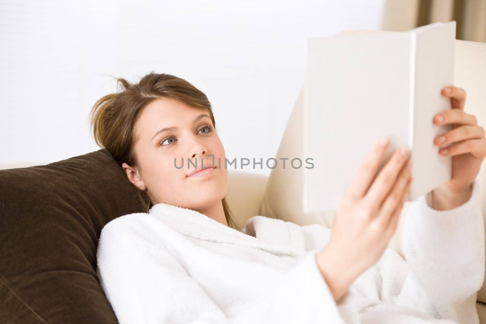 Young woman read book on sofa wearing bathrobe