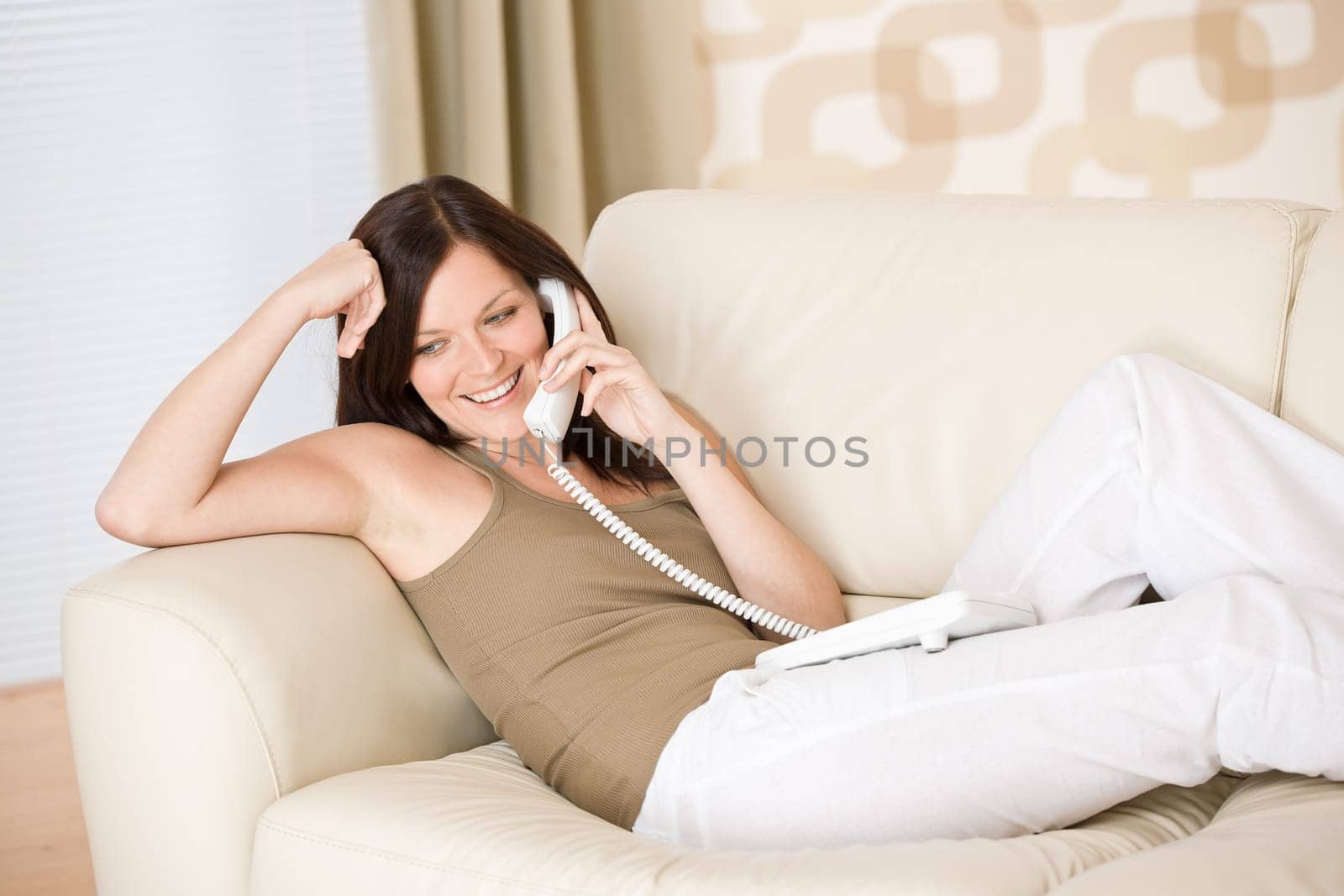 On the phone home - Smiling woman on sofa calling