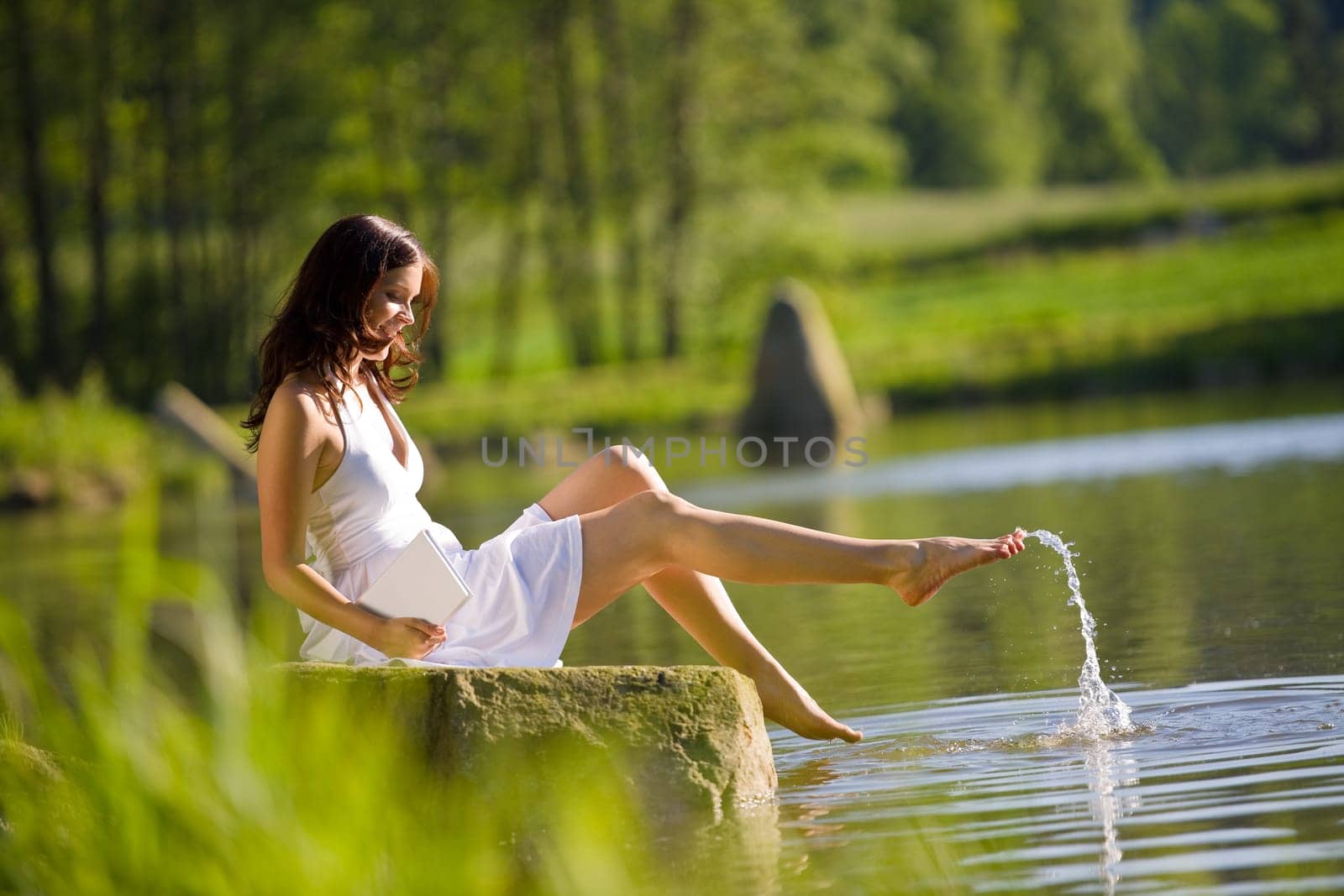 Happy romantic woman sitting by lake splashing water