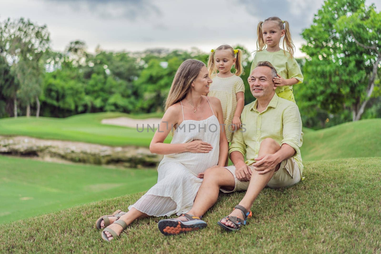 A happy family, two girls, dad, and a pregnant mom, enjoys quality time together on a lush green lawn, creating cherished memories of togetherness by galitskaya