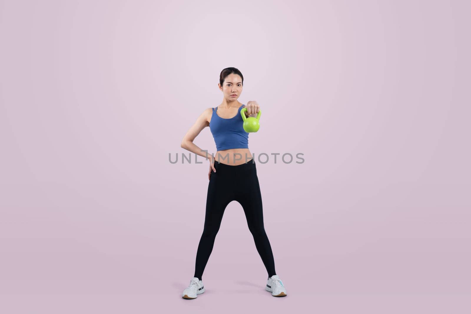 Vigorous energetic woman doing kettlebell weight lifting exercise on isolated background. Young athletic asian woman strength and endurance training session as body workout routine.