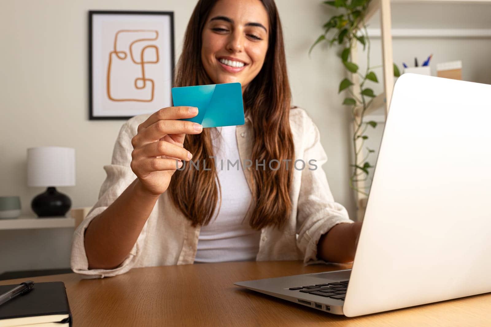 Happy caucasian woman using laptop and credit cart to shop online at home office. Selective focus on hand. by Hoverstock