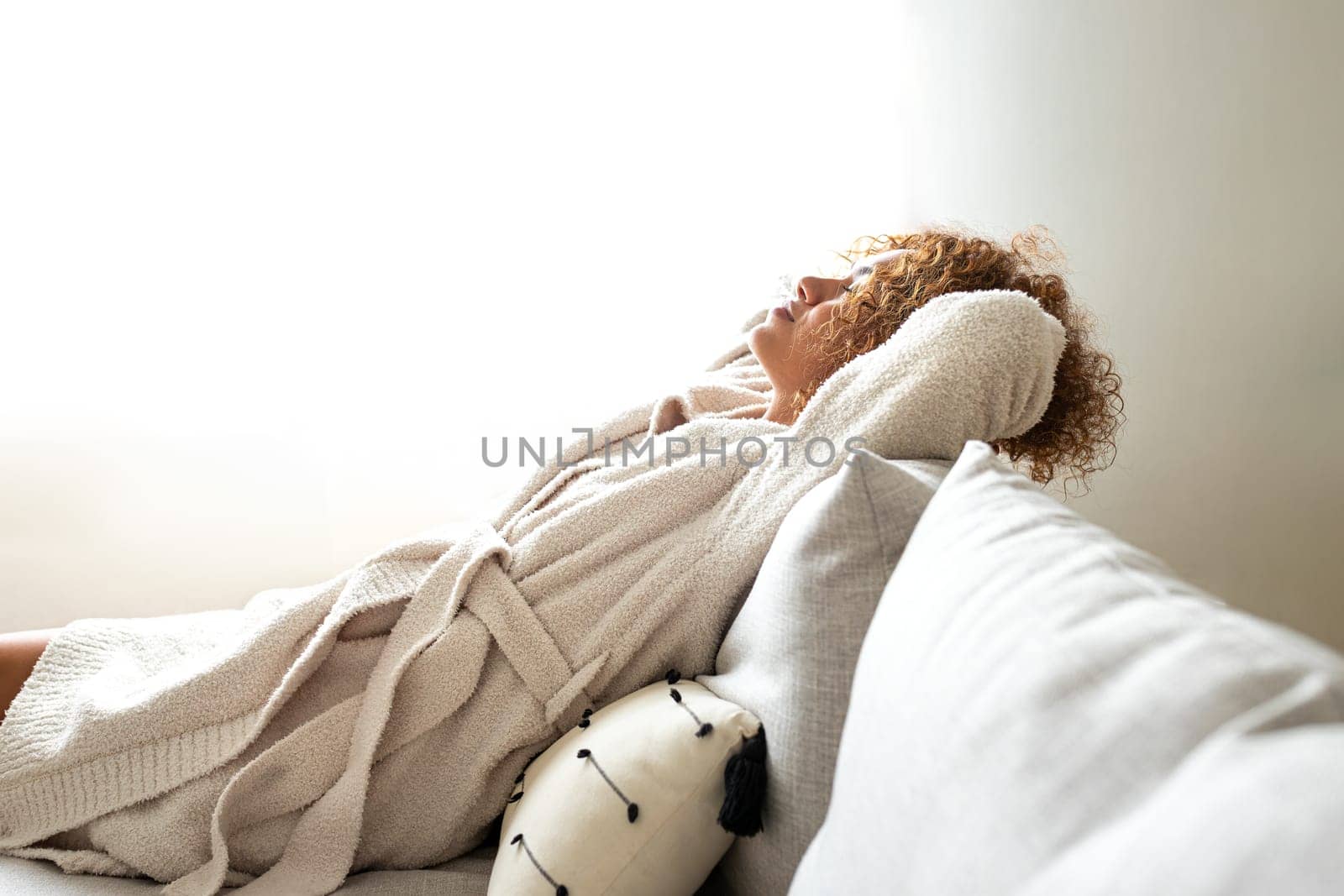 Side view of multiracial woman resting with arms behind the head sitting on the couch at home cozy living room. Copy space. Lifestyle concept.