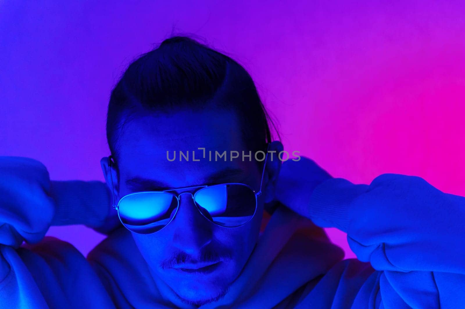 Portrait of a millennial man in neon light. Hipster in a hoodie. Selective focus