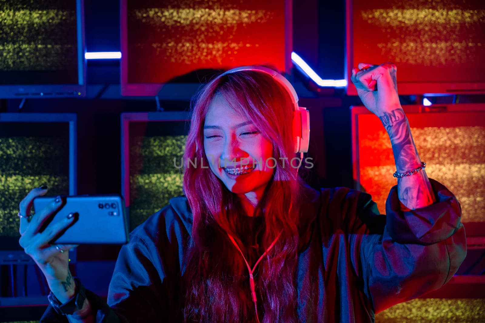 Winning. Young woman feeling excited at gaming room, Happy gamer people playing video game online with smart mobile phone with neon lights raising hands to wins celebrating, smile with smartphone