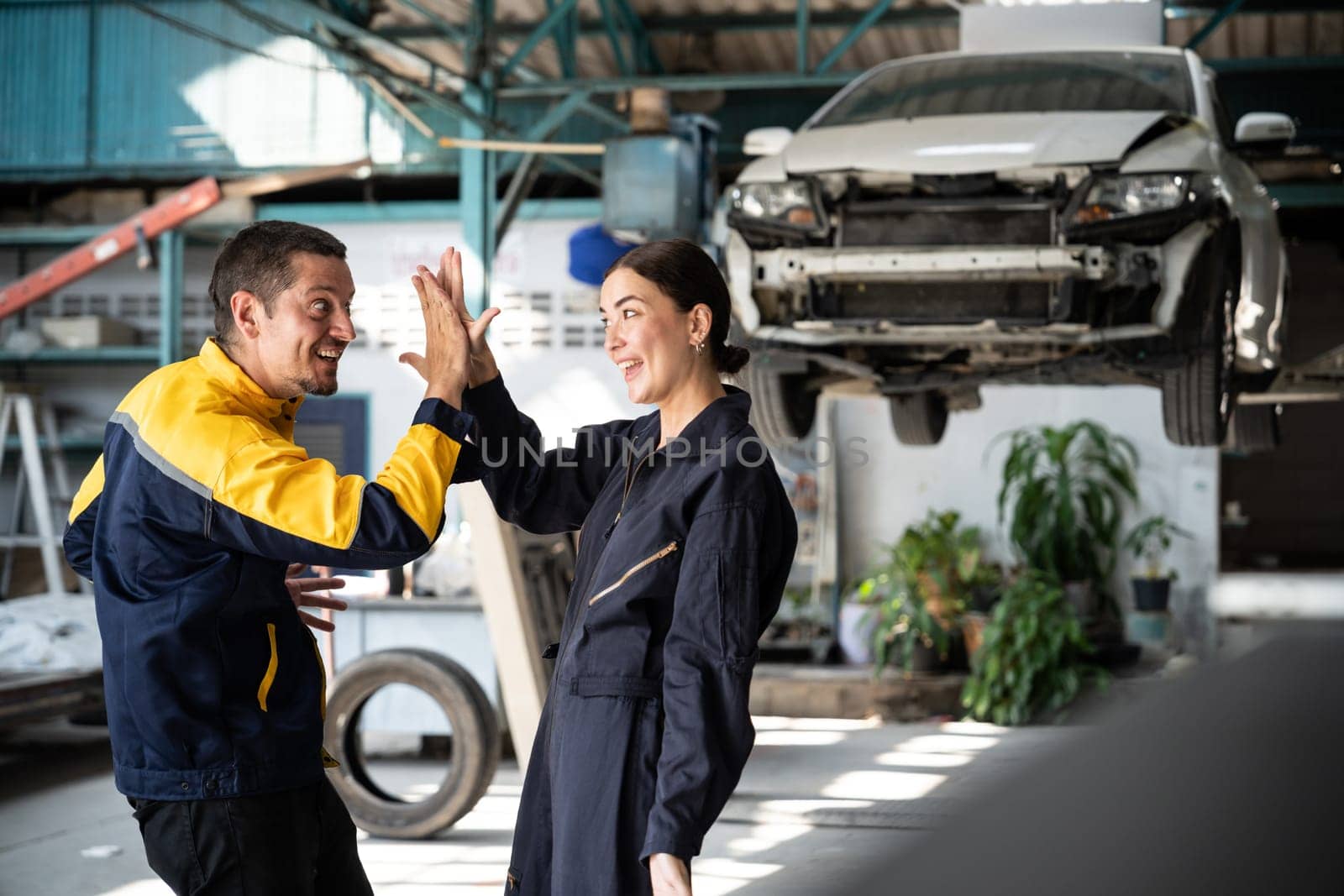 Two happy vehicle mechanic celebrate and high five after made successful car inspection or repair in automotive service car workshop. Technician team enjoy accomplishment together in garage. Oxus