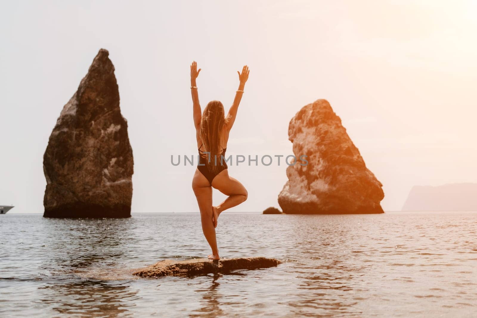 Woman sea yoga. Back view of free calm happy satisfied woman with long hair standing on top rock with yoga position against of sky by the sea. Healthy lifestyle outdoors in nature, fitness concept. by panophotograph