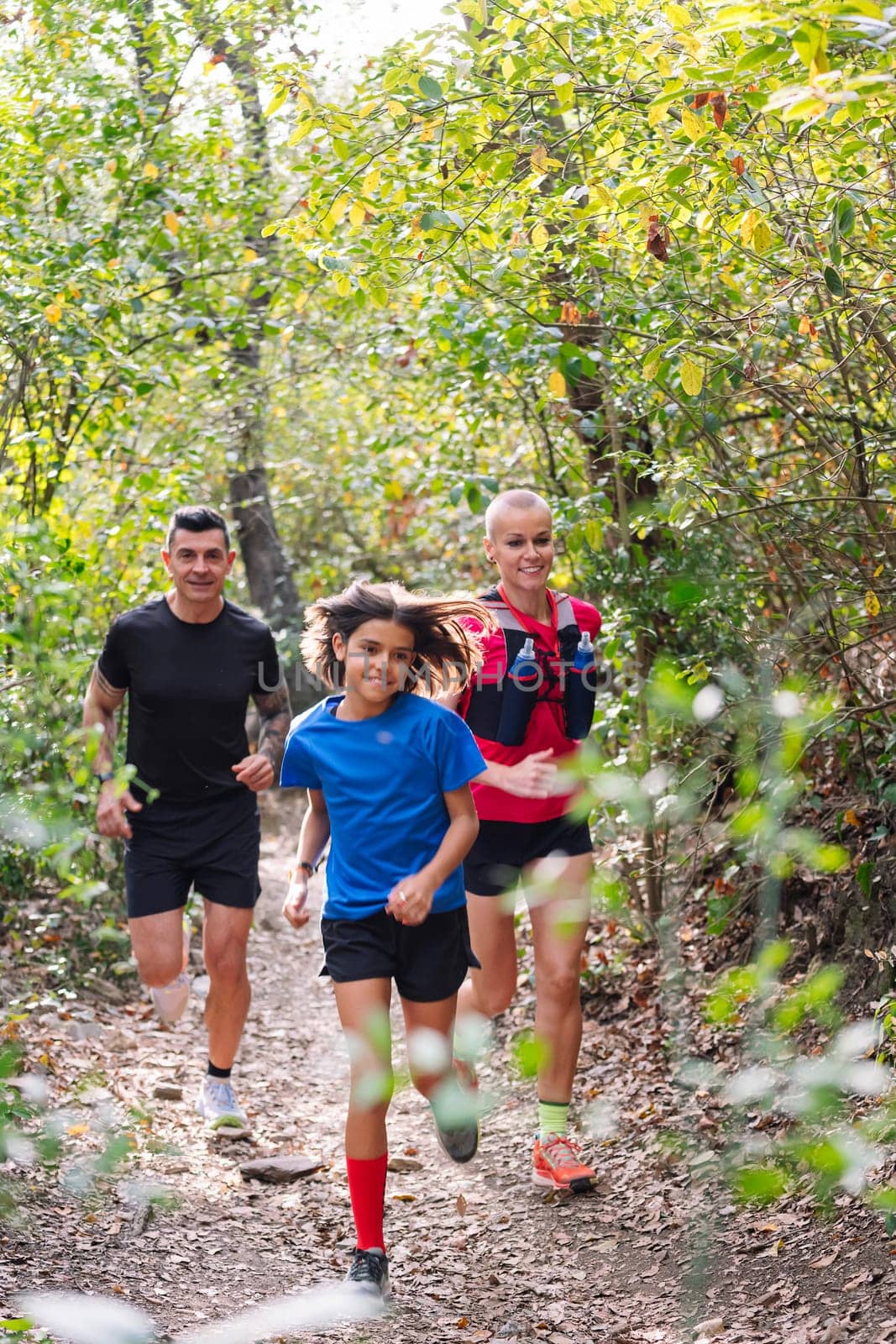 vertical photo of a family practicing trail running through the woods, concept of sport in nature and healthy family lifestyle, copy space for text