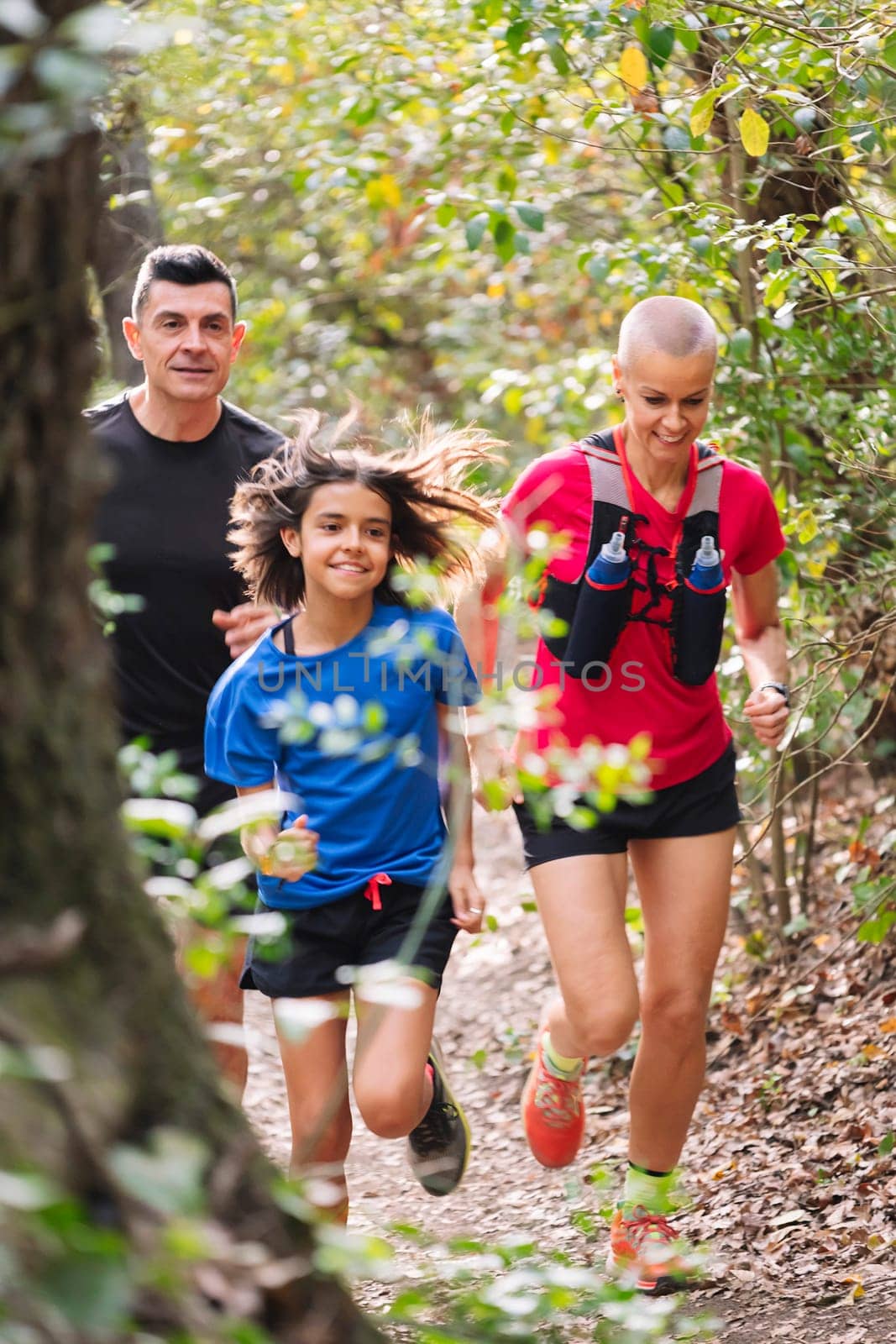 vertical photo of a family practicing trail running through the forest, concept of sport in nature and healthy family lifestyle, copy space for text