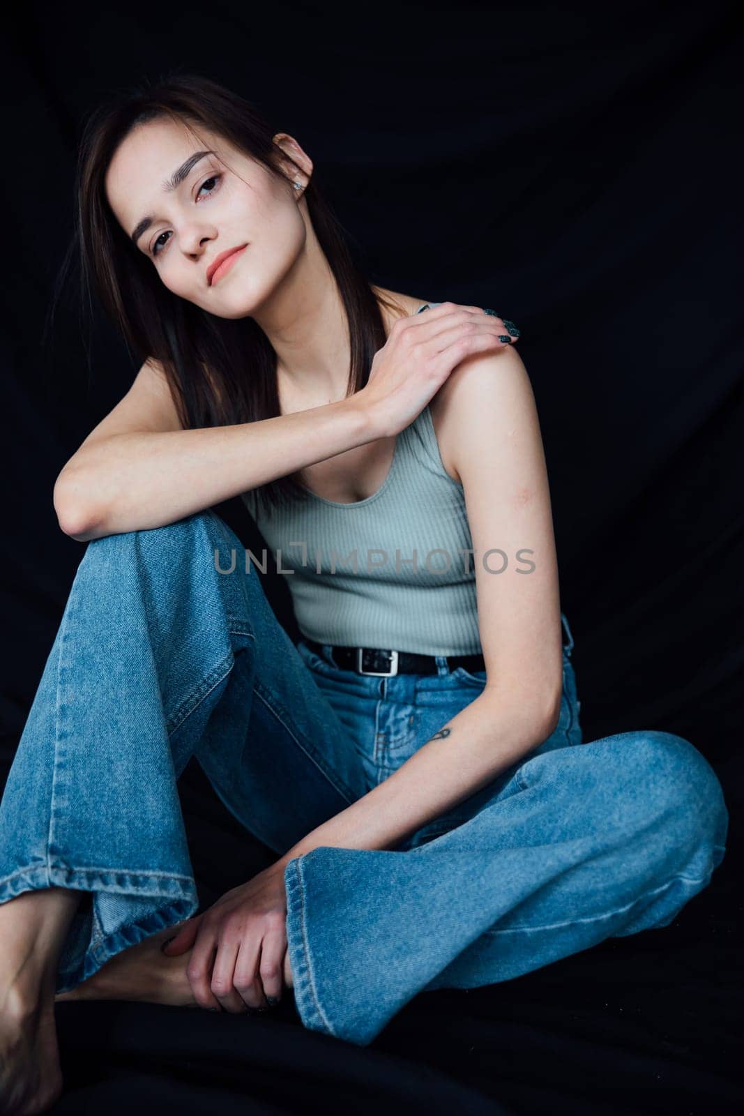 woman in denim pants sits on a chair on a black background