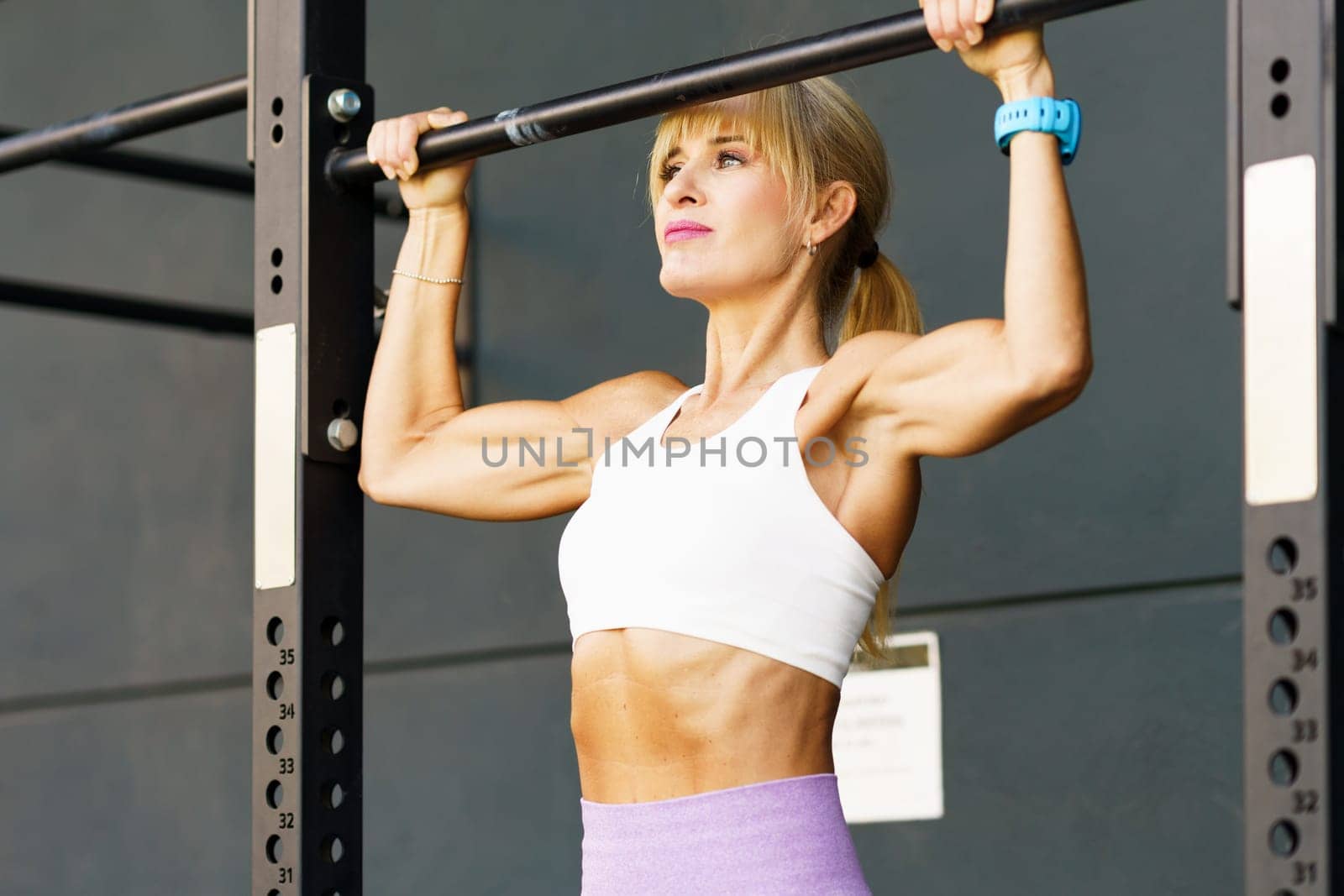 Muscular young female athlete in sportswear doing pull ups on bar during fitness workout at gym leading healthy lifestyle