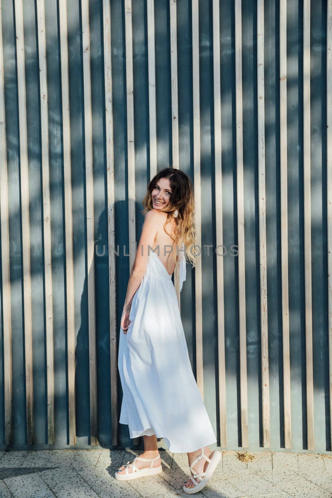 woman in a white dress stands against a wooden wall in a park on the street walk