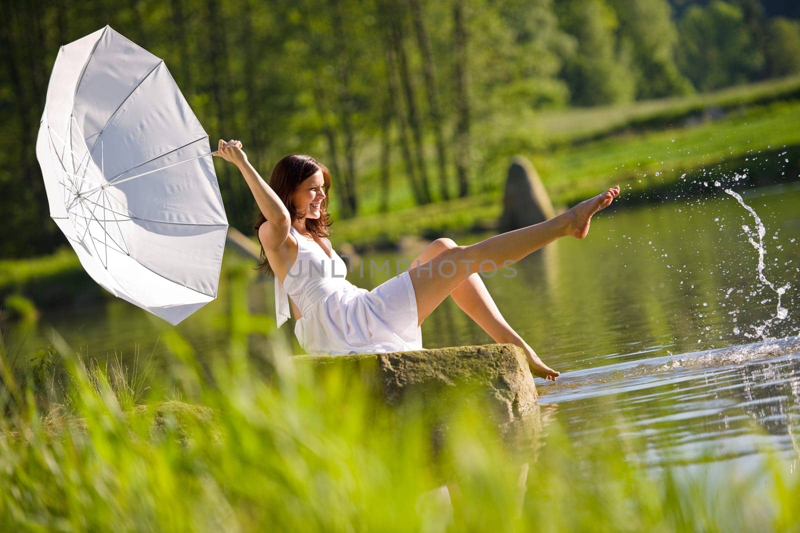 Happy romantic woman sitting by lake splashing water