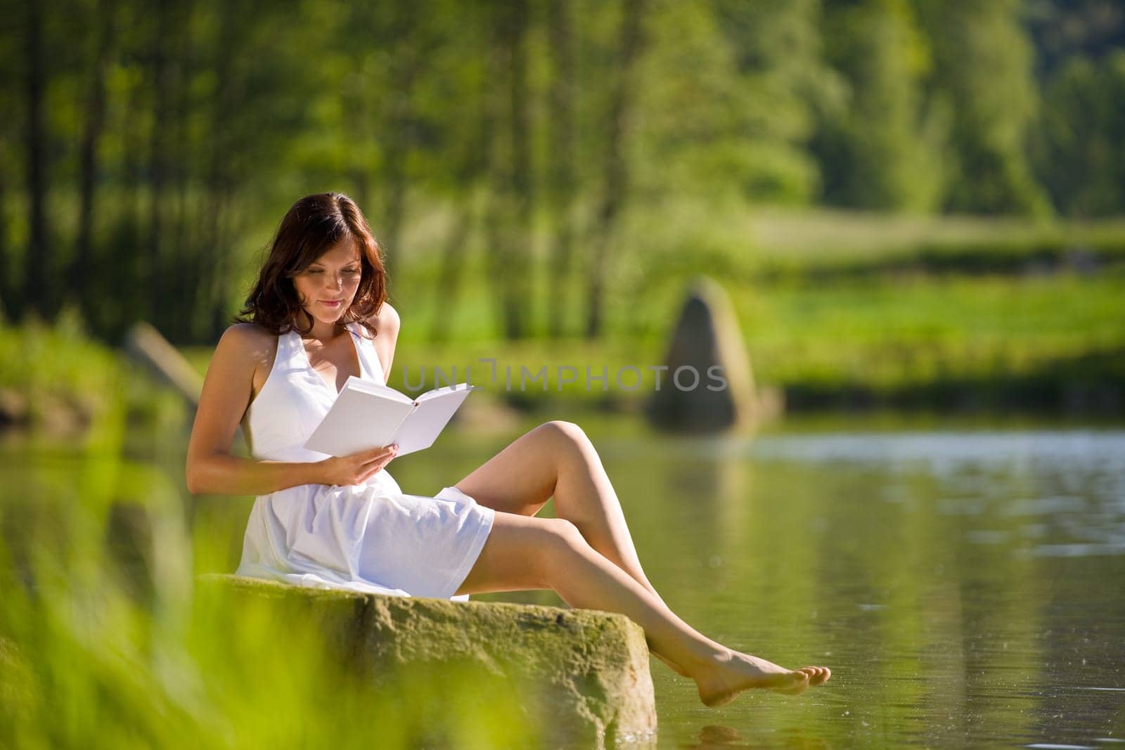 Happy romantic woman sitting by lake with book