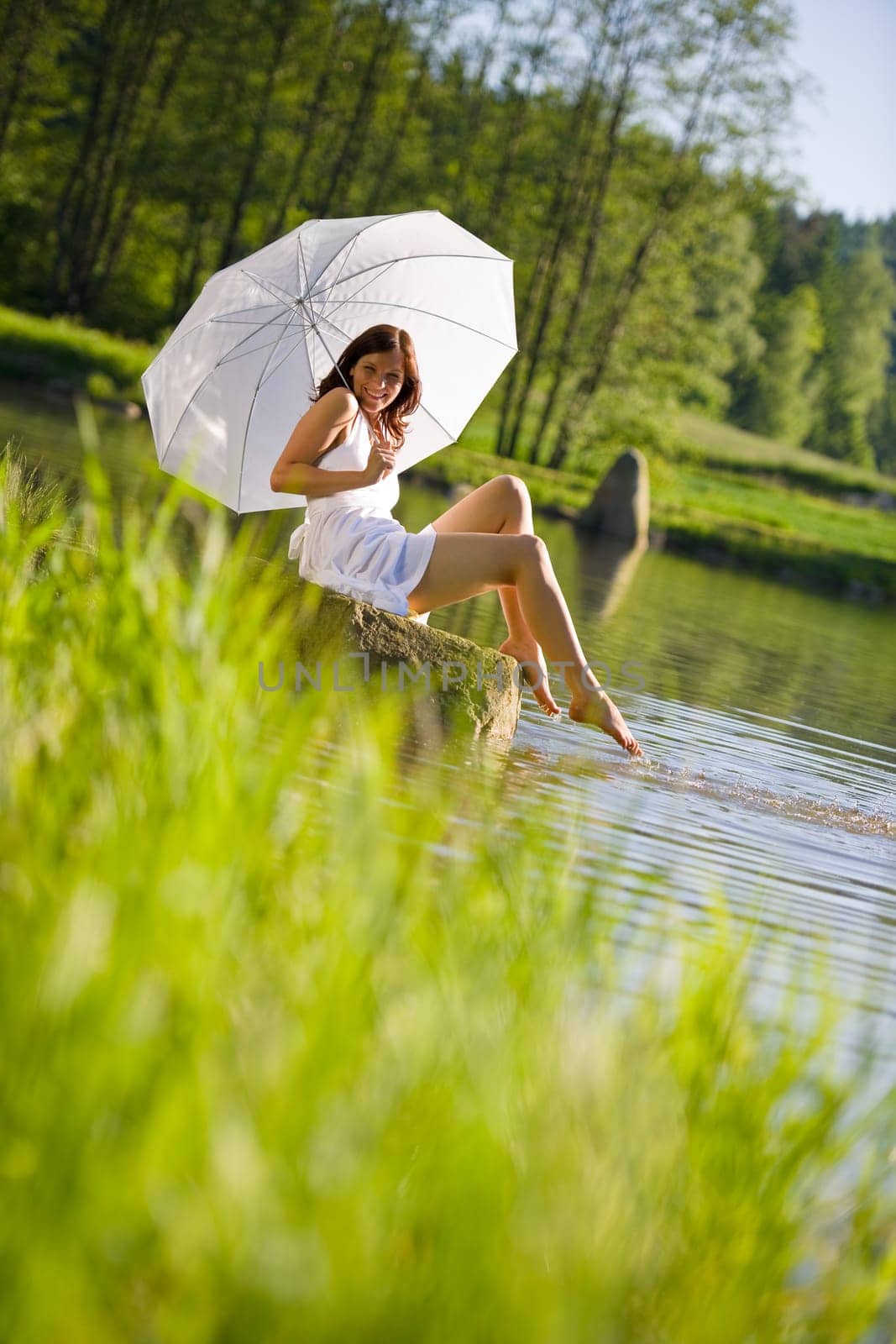 Happy romantic woman sitting by lake splashing water