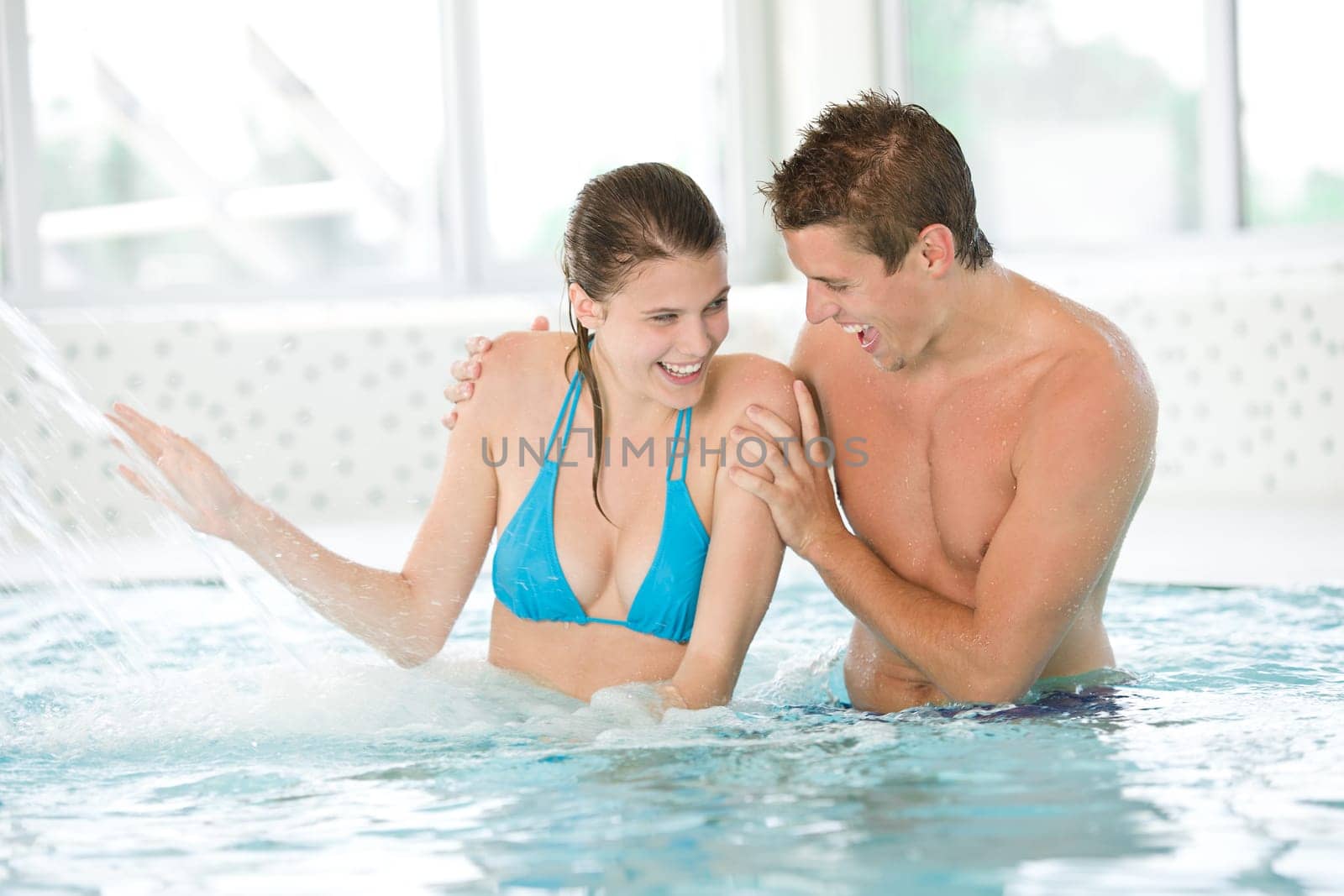 Young loving couple have fun under water stream in pool