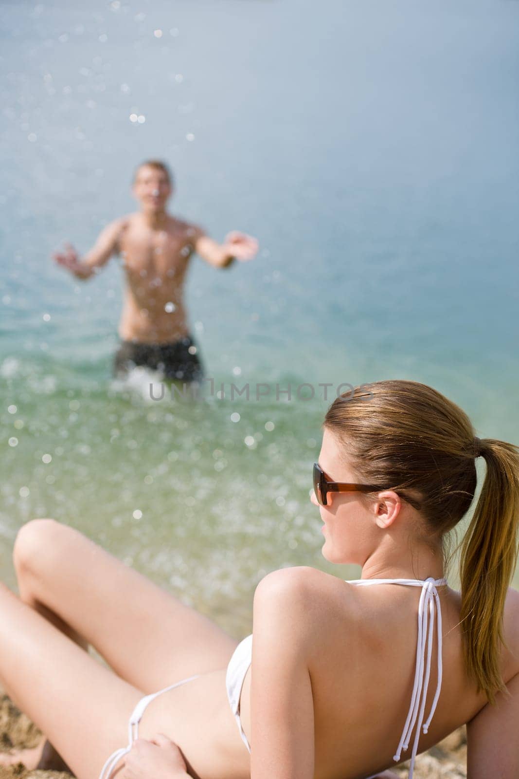 Couple on beach woman in bikini sunbathe