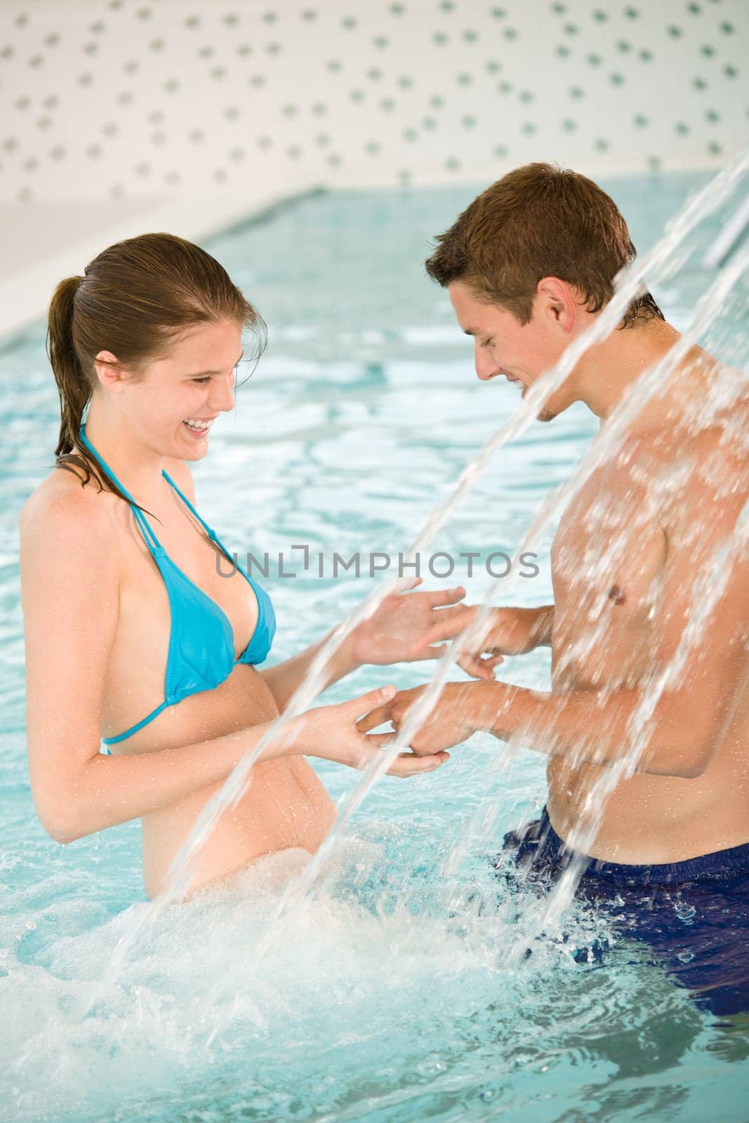 Swimming pool - young couple play under water stream