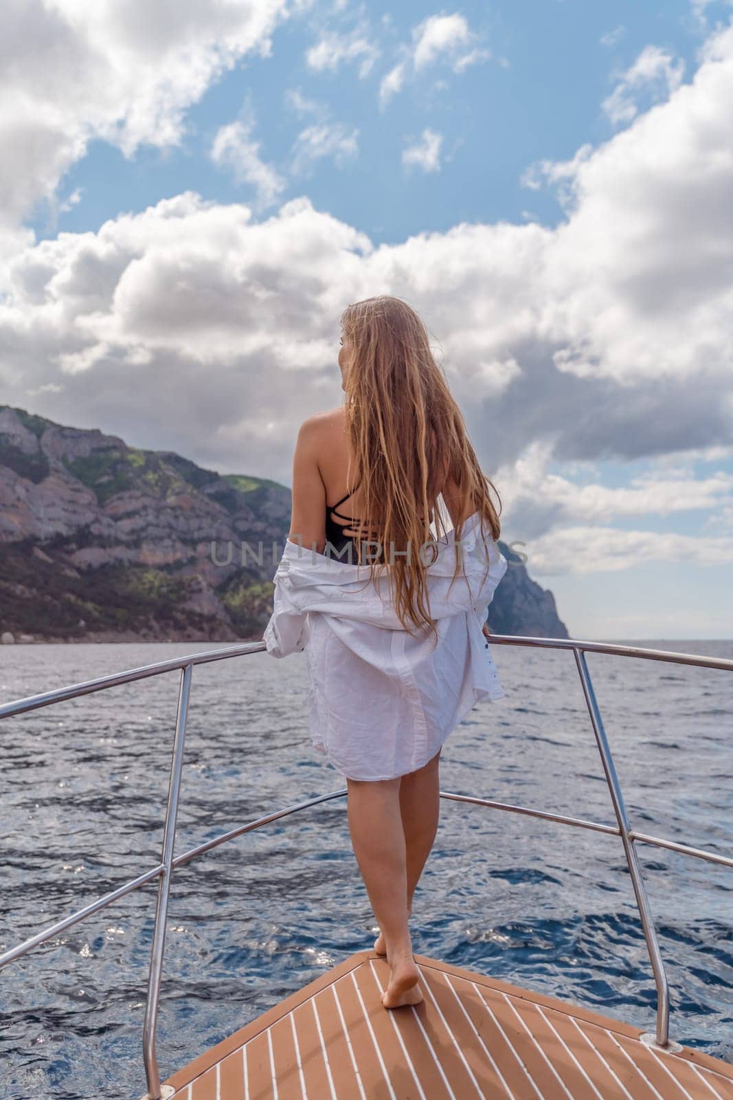 Woman on a yacht. Happy model in a swimsuit posing on a yacht against a blue sky with clouds and mountains.