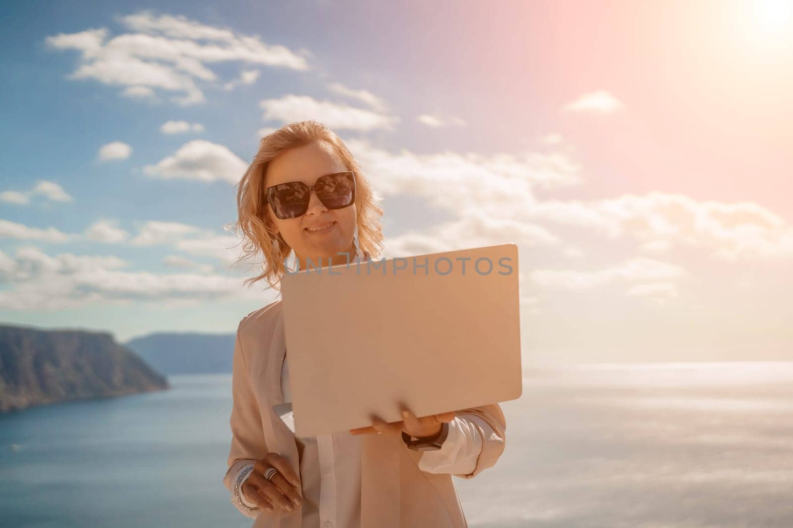 Freelance women sea. She is working on the computer. Good looking middle aged woman typing on a laptop keyboard outdoors with a beautiful sea view. The concept of remote work