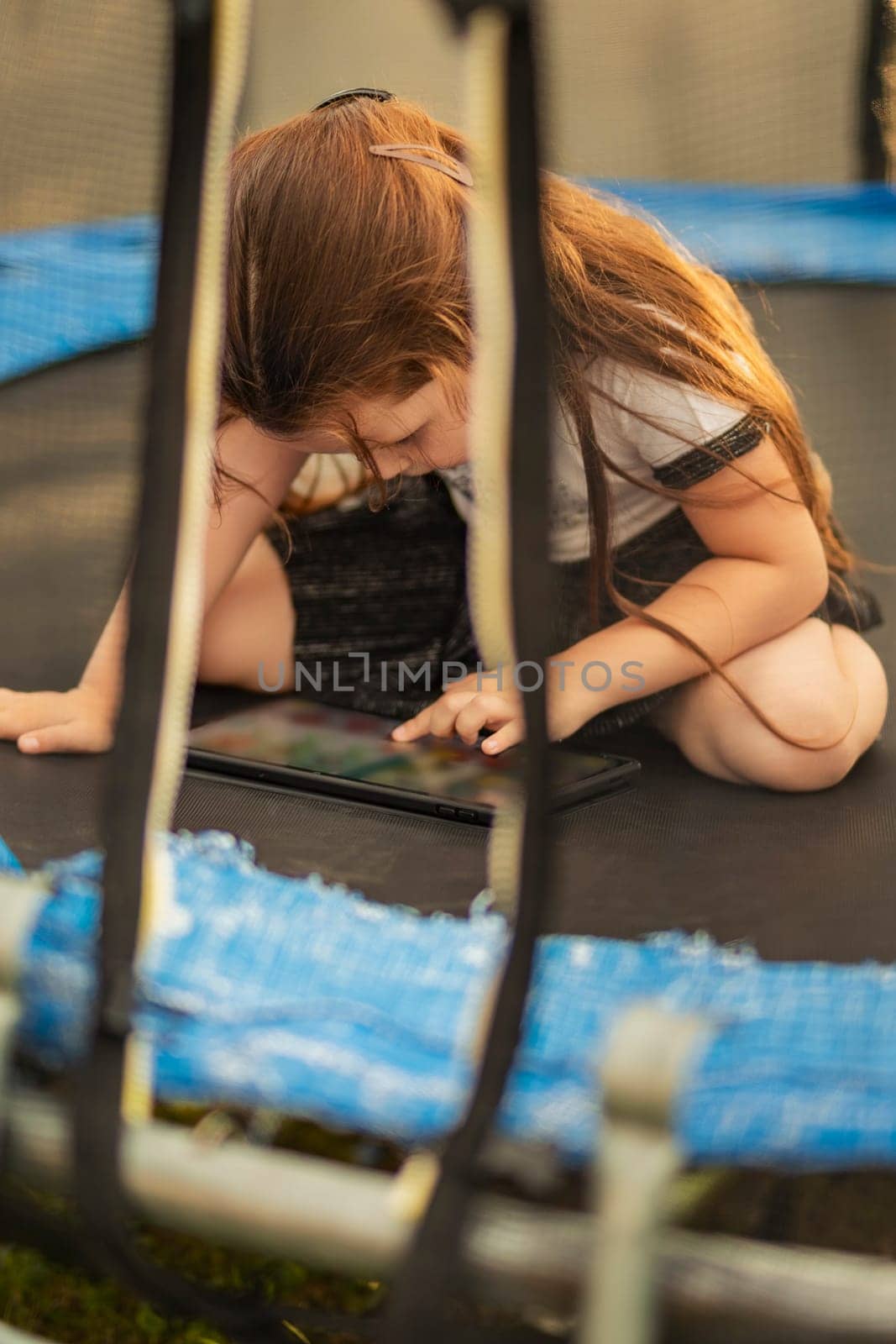girl sitting on a trampoline and playing on a tablet by zokov
