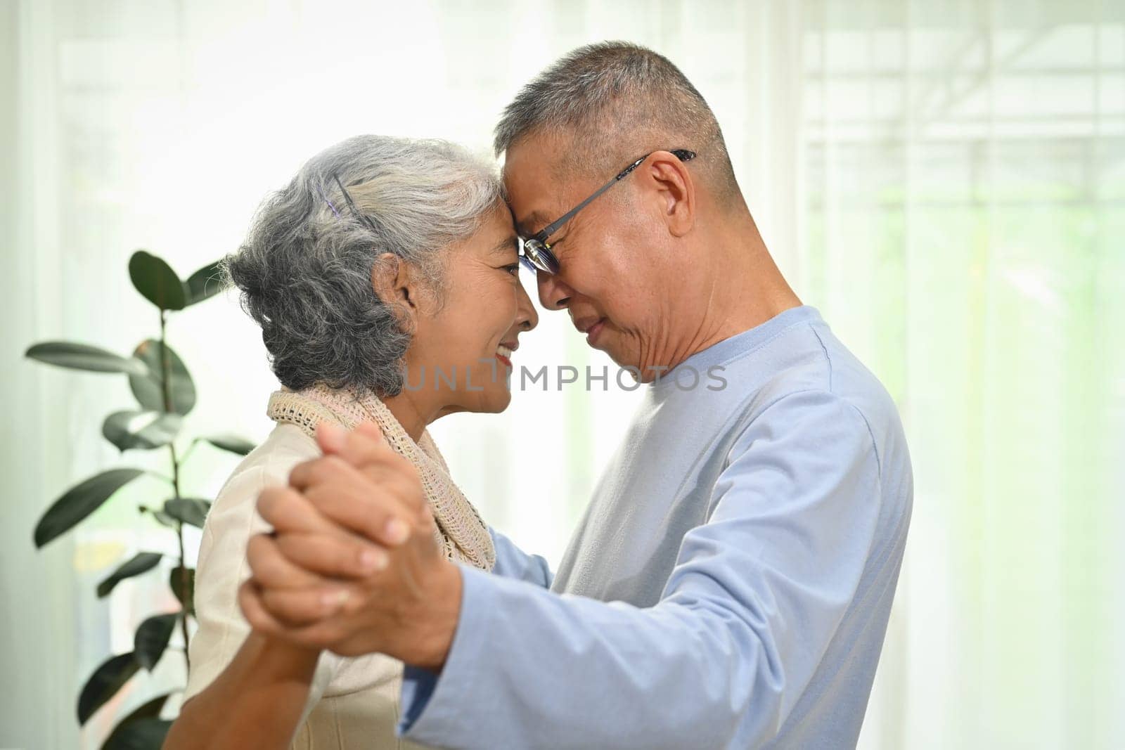 Happy elderly couple spouses dancing in living room while spending time together at home by prathanchorruangsak