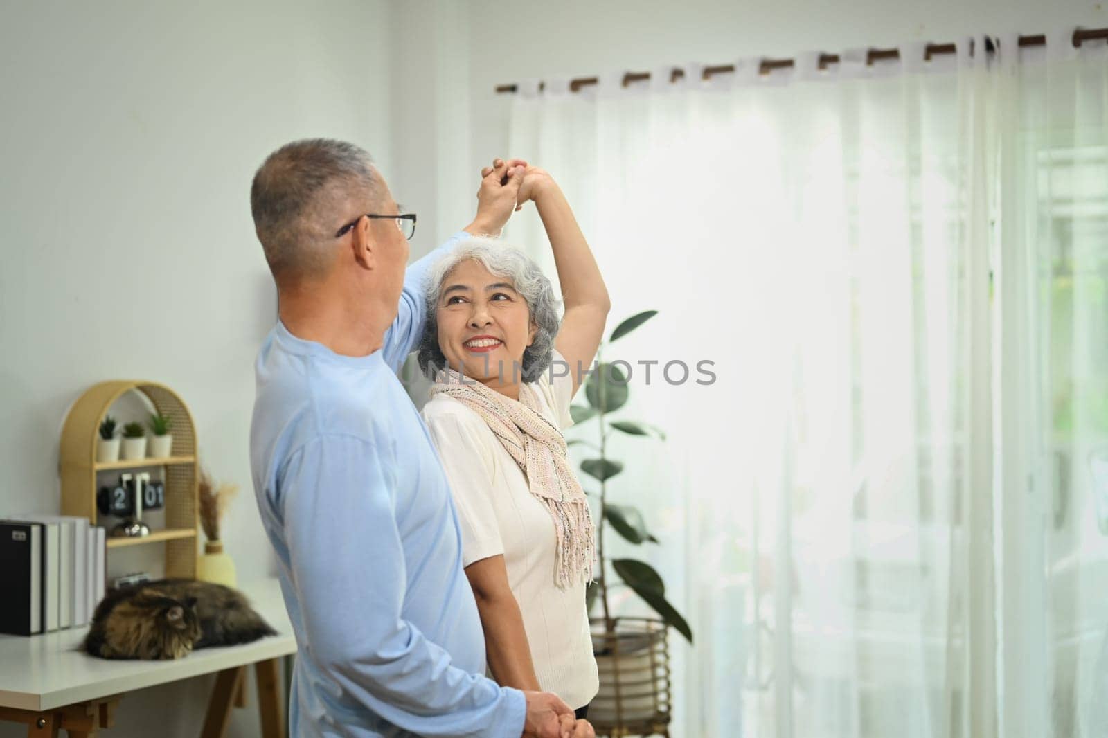 Overjoyed elderly male and female pensioner having fun dancing in living room. Retirement lifestyle concept.