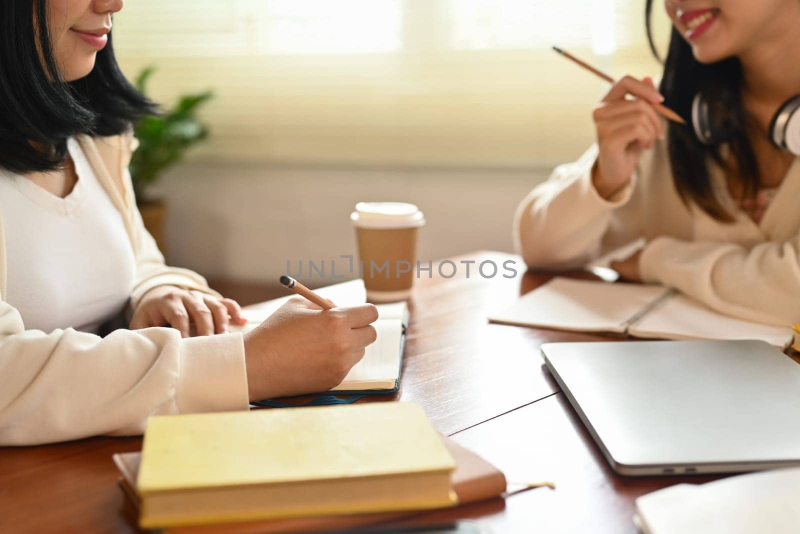 Two female students studying and preparing for exam in college library. Education and youth lifestyle concept by prathanchorruangsak