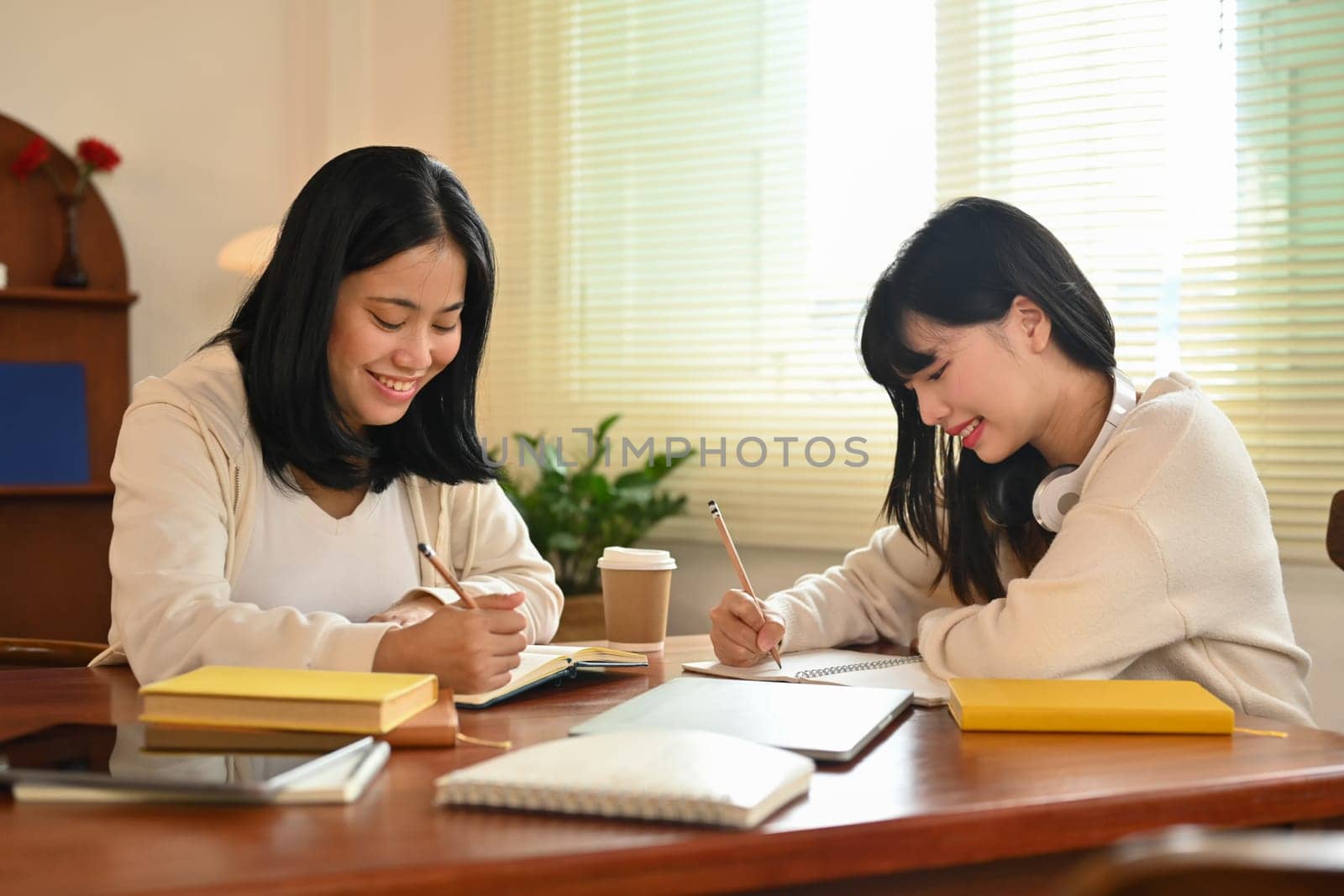 Two smiling university student discussing their home assignment in library. Education and lifestyle concept by prathanchorruangsak