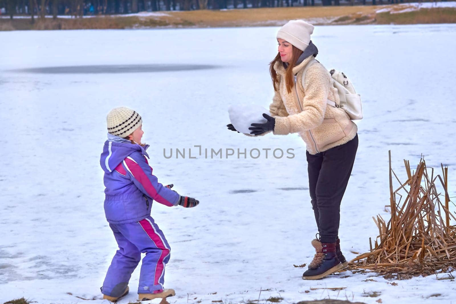 Cute mother playing with snowballs with her child on a walk on a frozen lake by jovani68