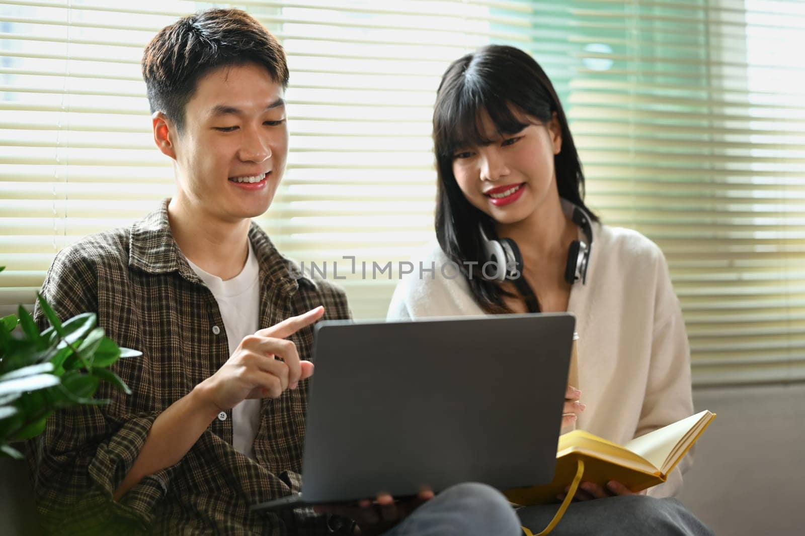 Smiling asian male student doing group project with his classmate on laptop. Education and youth lifestyle concept by prathanchorruangsak