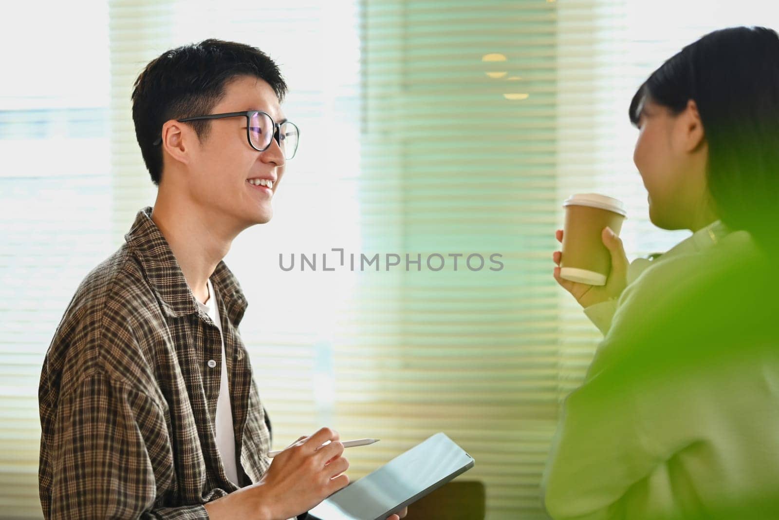 Friendly male student in glasses checking university schedule on digital tablet and talking with his friend.