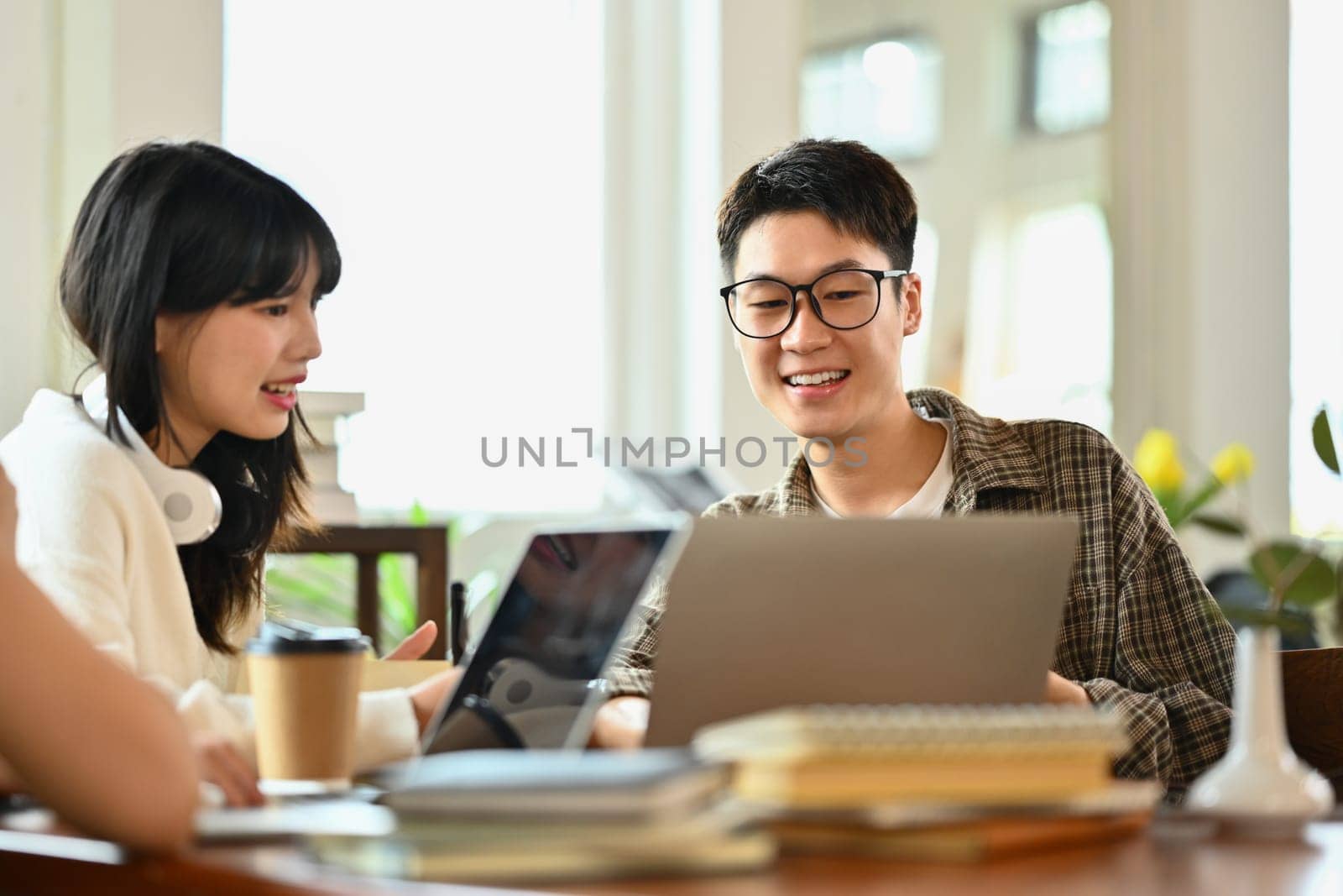 Friendly asian man student doing group project or preparing presentation on laptop with classmates by prathanchorruangsak