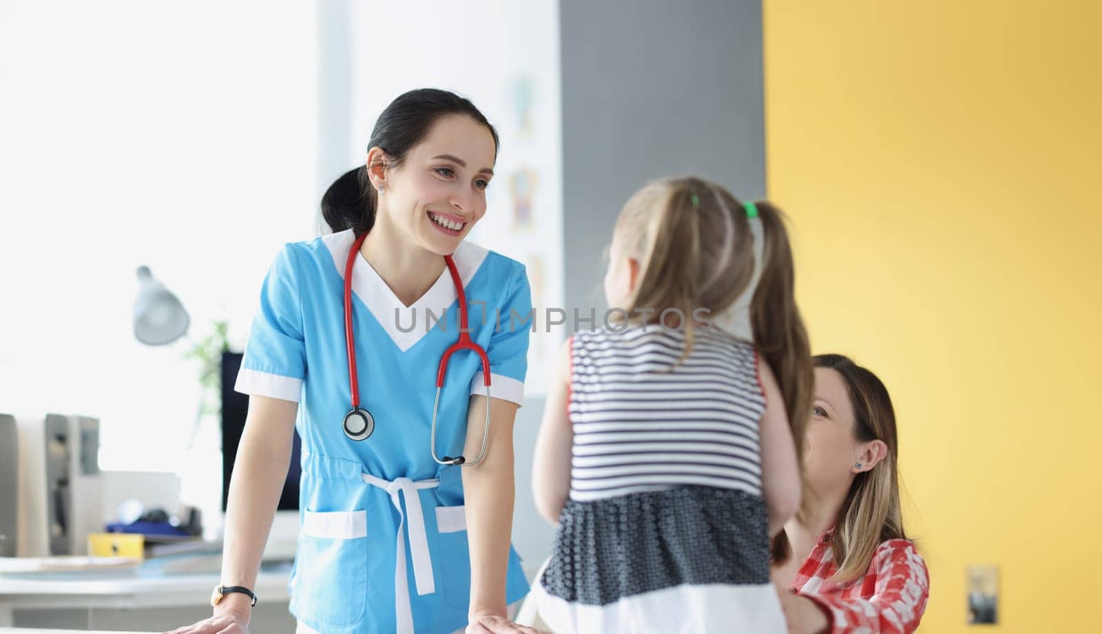 Pretty pediatrician chatting with cute patient child girl on appointment in clinic by kuprevich