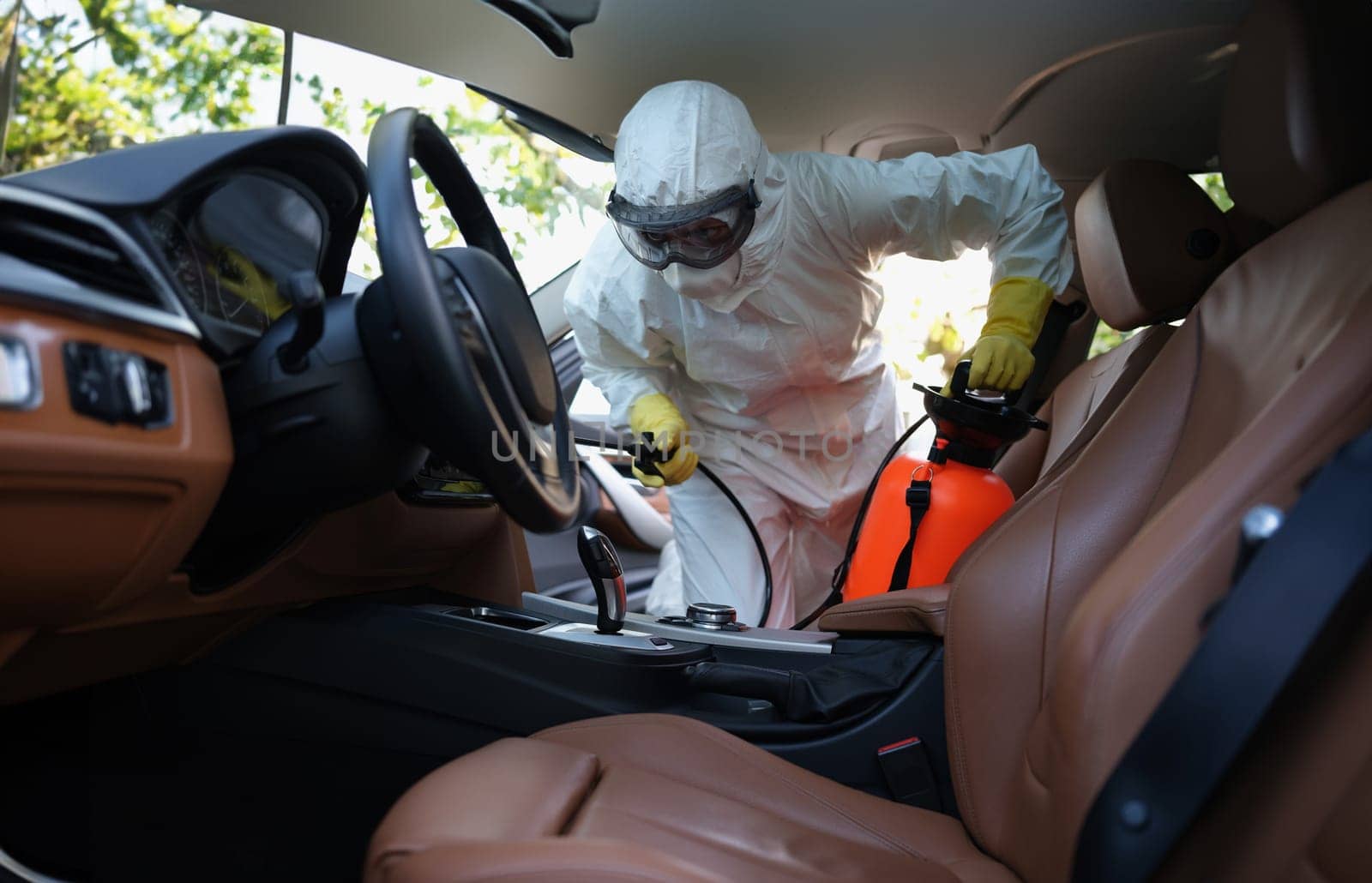 Portrait of worker in uniform cleanse car interior with spray disinfectant in container. Disinfect machine upholstery from infection. Covid prevent concept