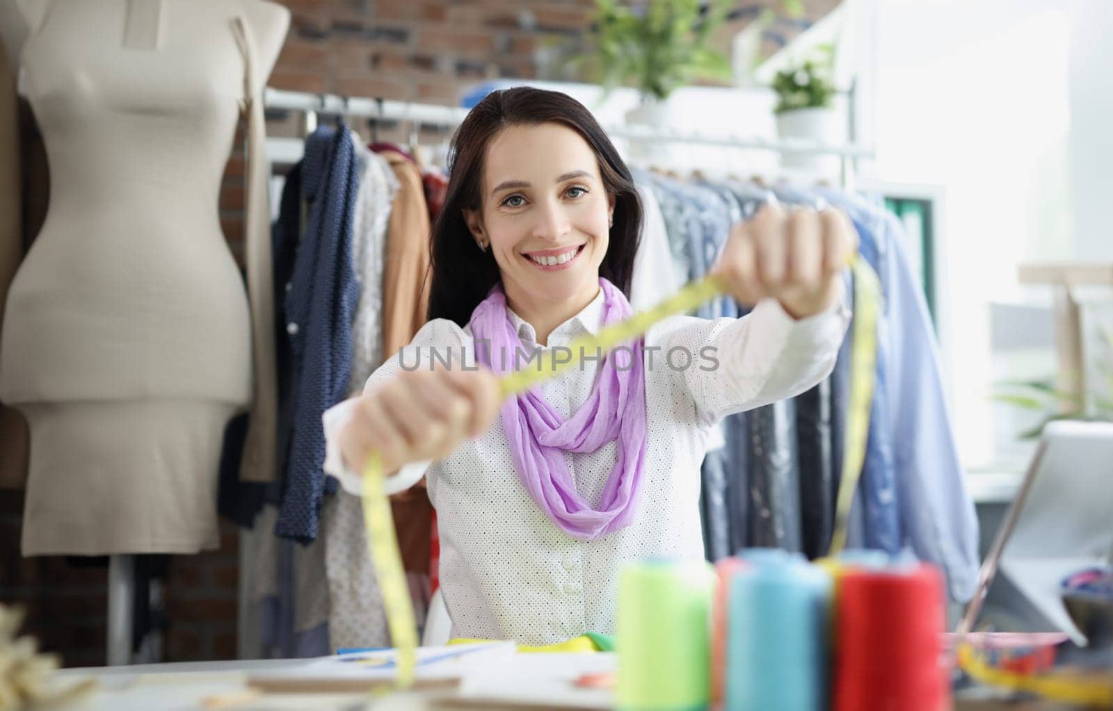 Portrait of smiling dressmaker woman willing to tape measure you, find out clothes size. Individual suit sewing, atelier. Fashion, business, hobby concept