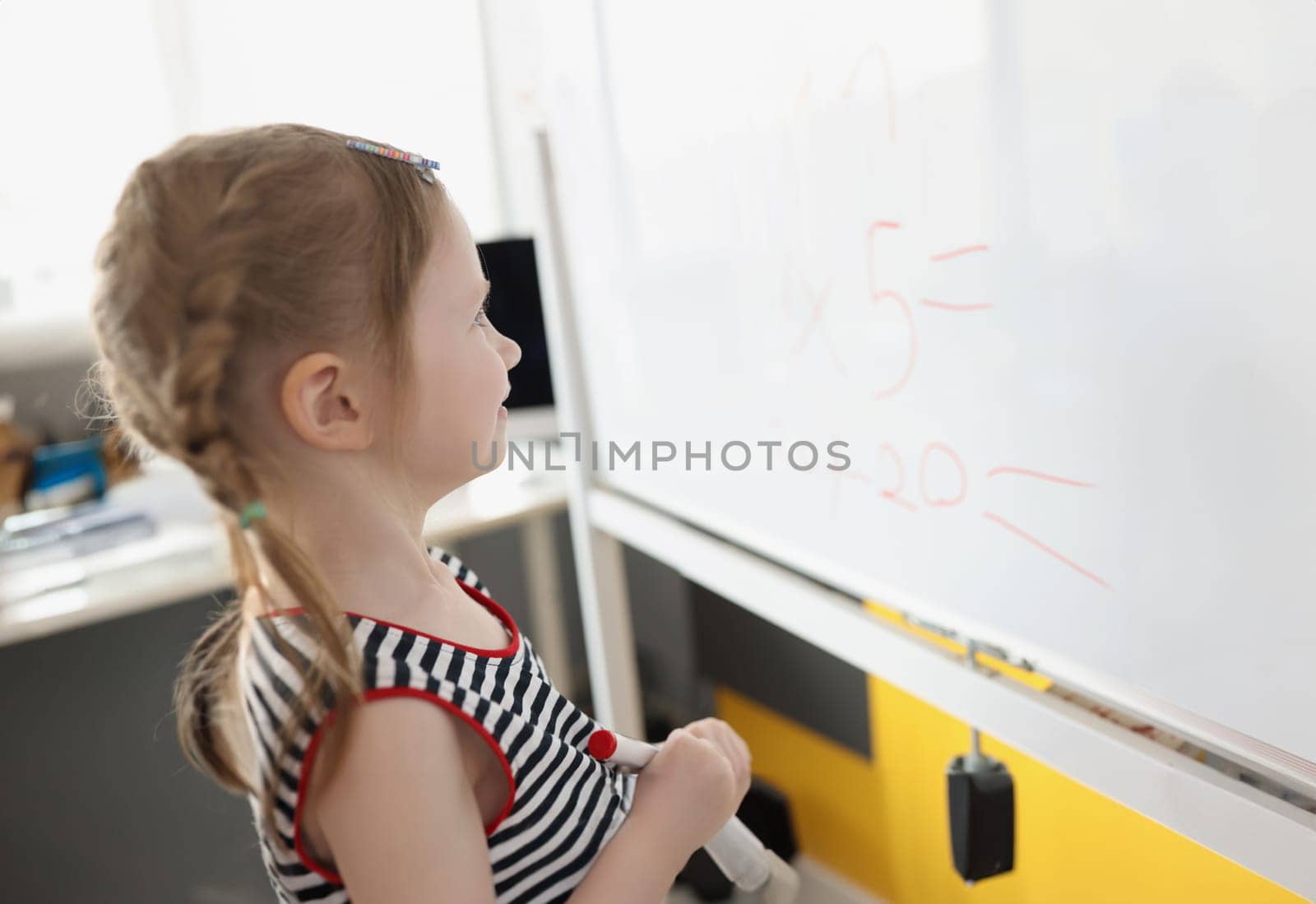 Portrait of toddler writing solution of sums on white board at school, educational process. School kid think while doing mathematics problem. Learn concept