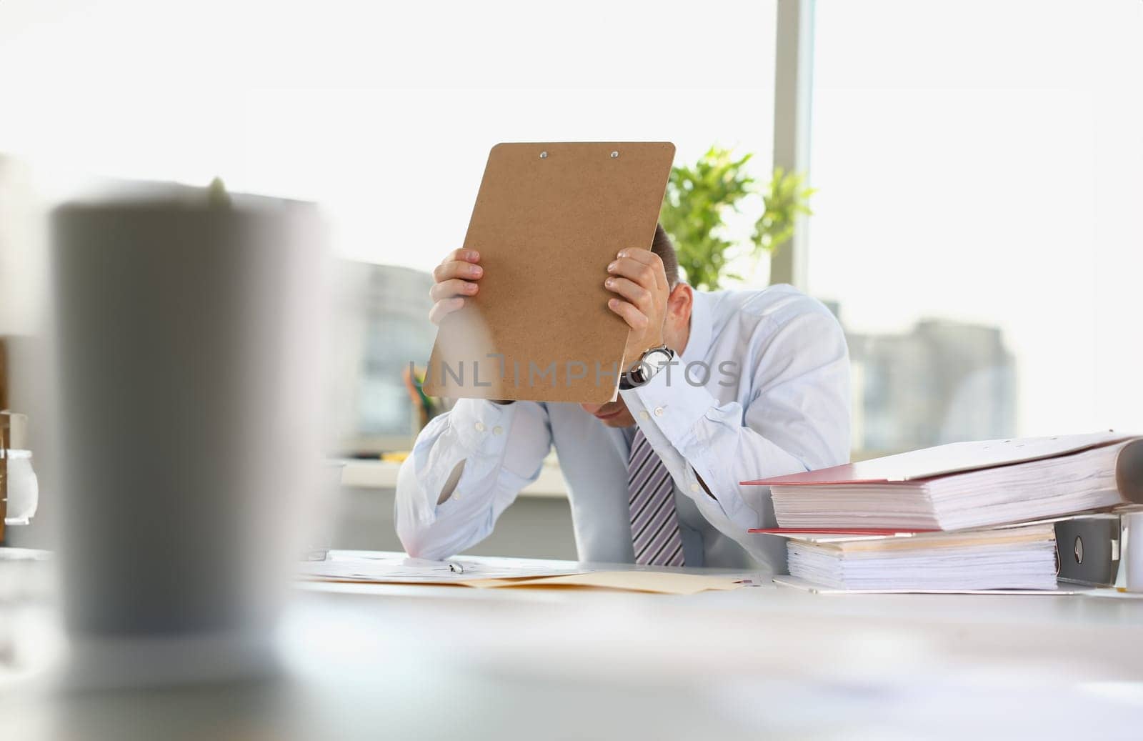 Portrait of tired overworked office clerk on workplace, stressful and exhausted male employee cover head with folder. Hardworker, job, deadline concept